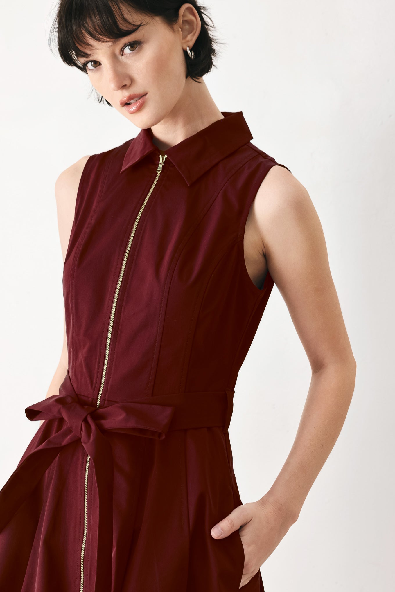 Woman wearing a burgundy red woven midi dress featuring collar, sleeveless, front zipper closure, self sash tie, pockets and full skirt | FREEMARKET
