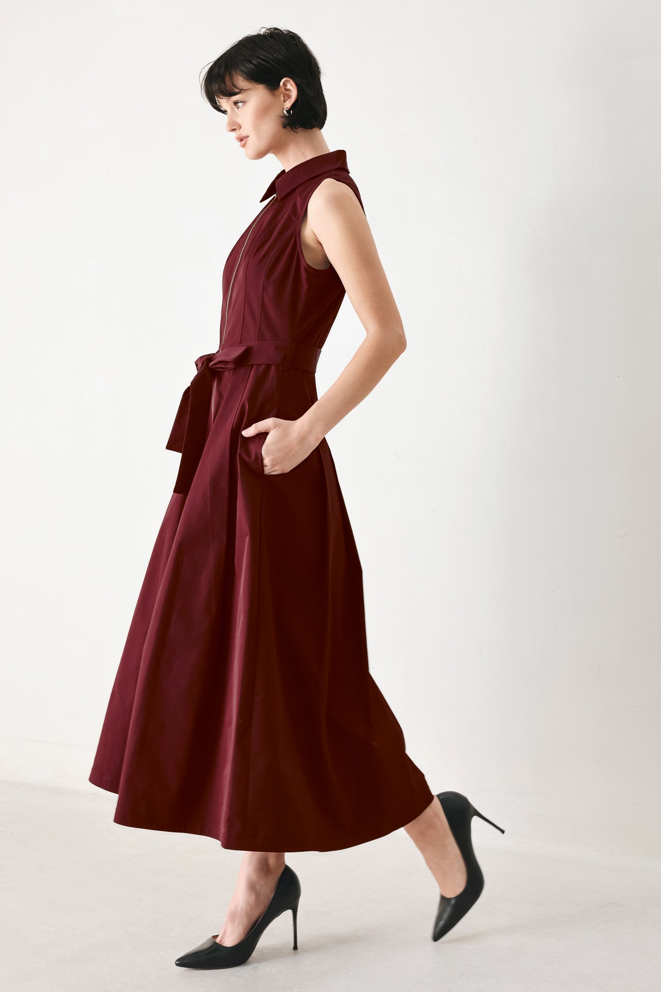 Woman wearing a burgundy red woven midi dress featuring collar, sleeveless, front zipper closure, self sash tie, pockets and full skirt | FREEMARKET