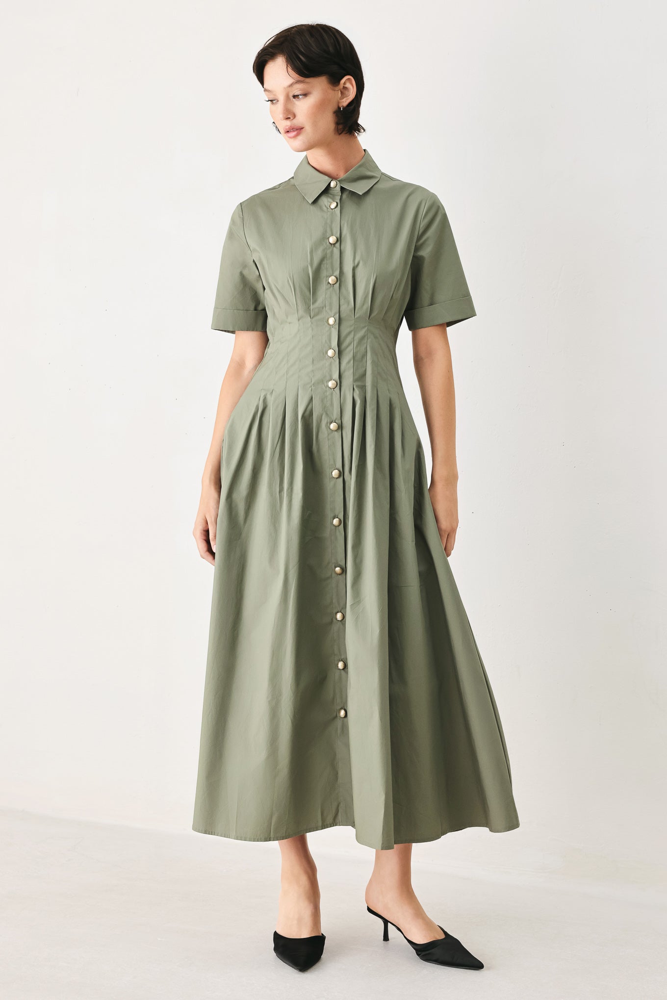Woman wearing an olive midi dress featuring collar, short sleeve, button down, corset waist, side pockets and full skirt | FREEMARKET