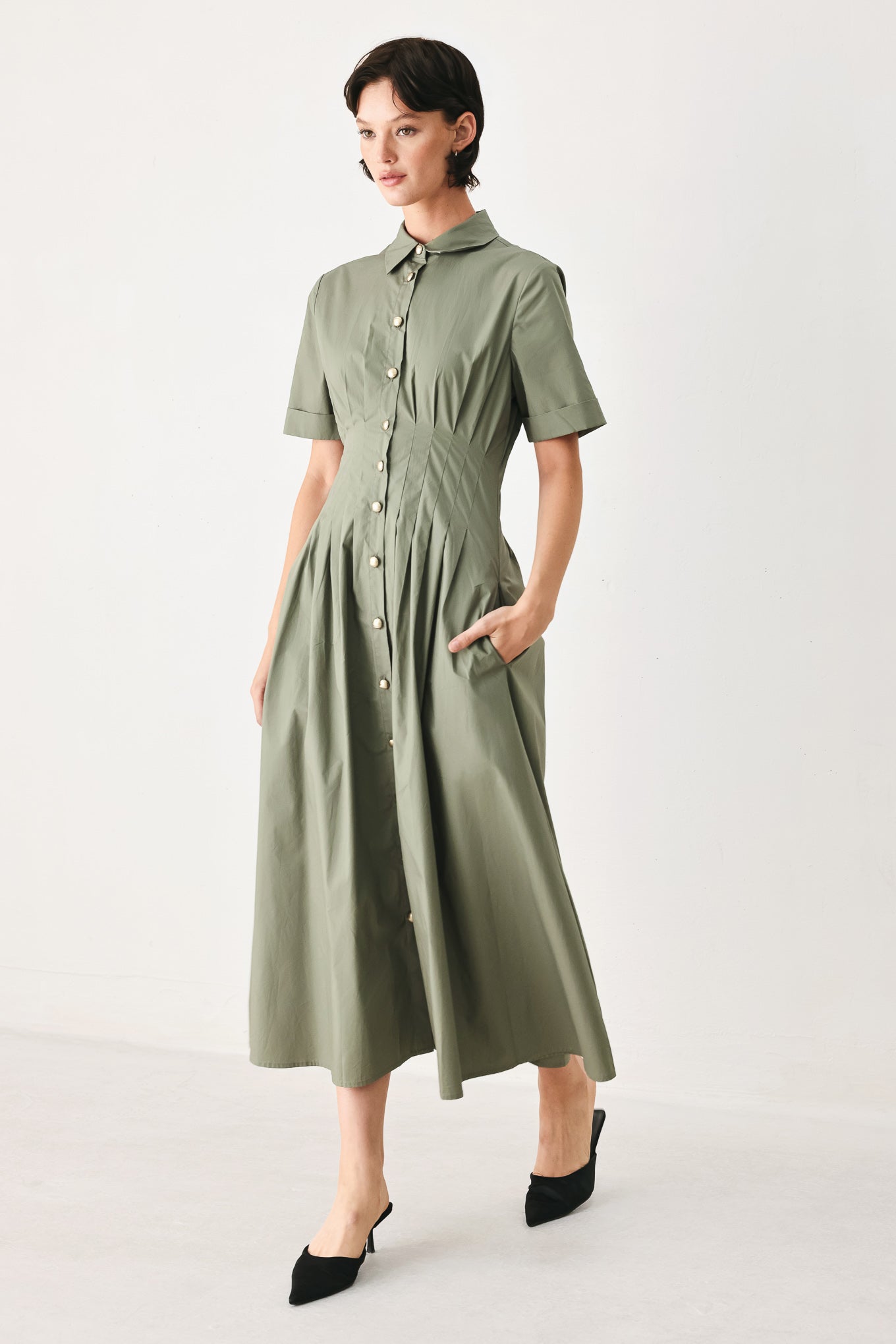 Woman wearing an olive midi dress featuring collar, short sleeve, button down, corset waist, side pockets and full skirt | FREEMARKET