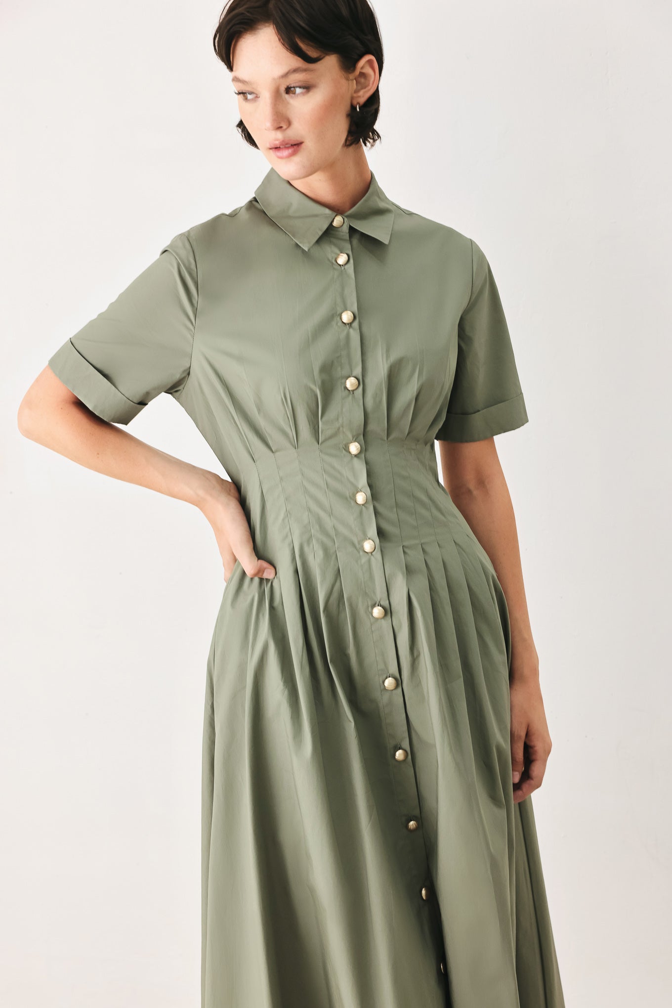 Woman wearing an olive midi dress featuring collar, short sleeve, button down, corset waist, side pockets and full skirt | FREEMARKET