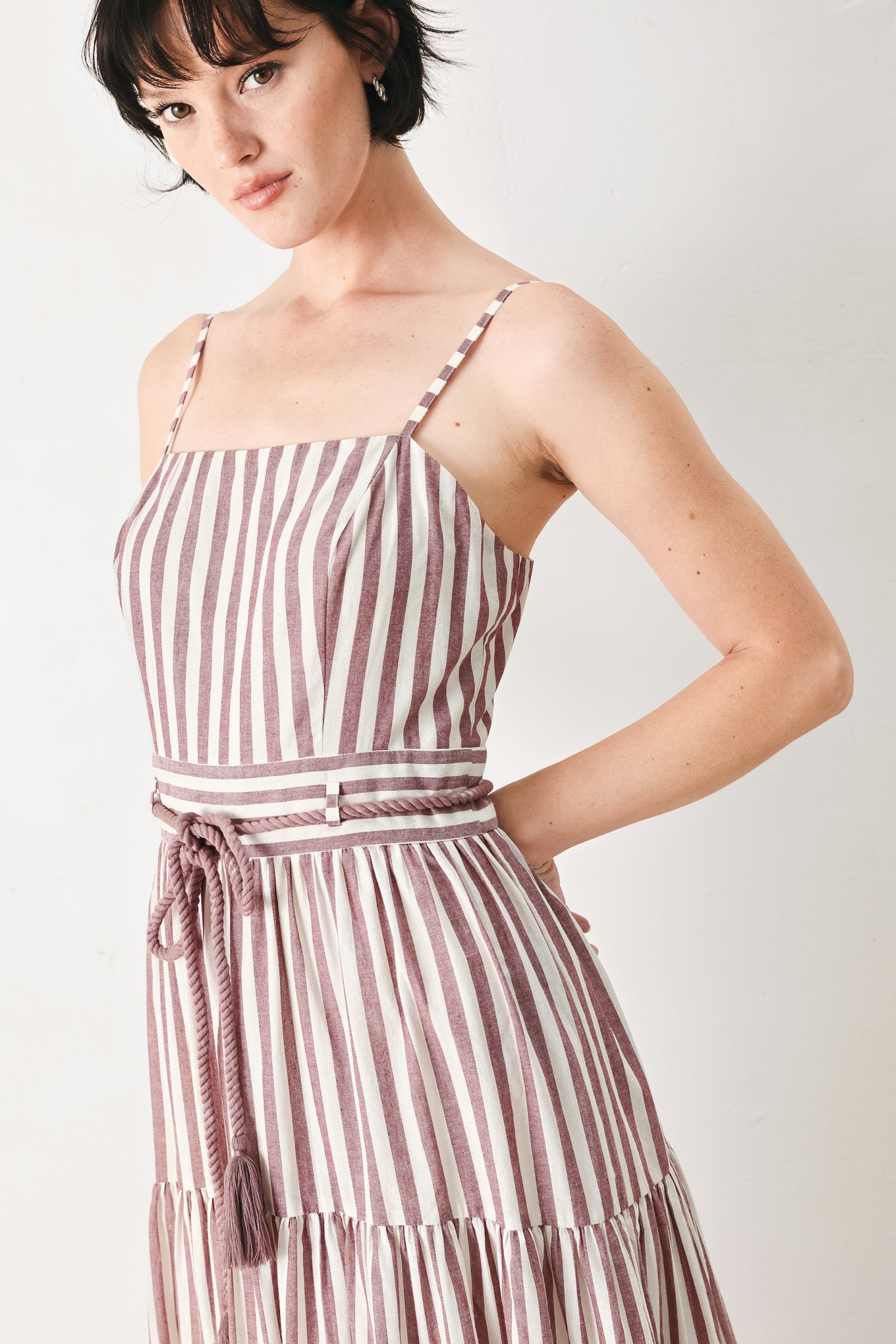 Woman wearing a burgundy striped woven ankle dress featuring straight neckline, straps, rope tie, tier skirt and back zipper closure | FREEMARKET