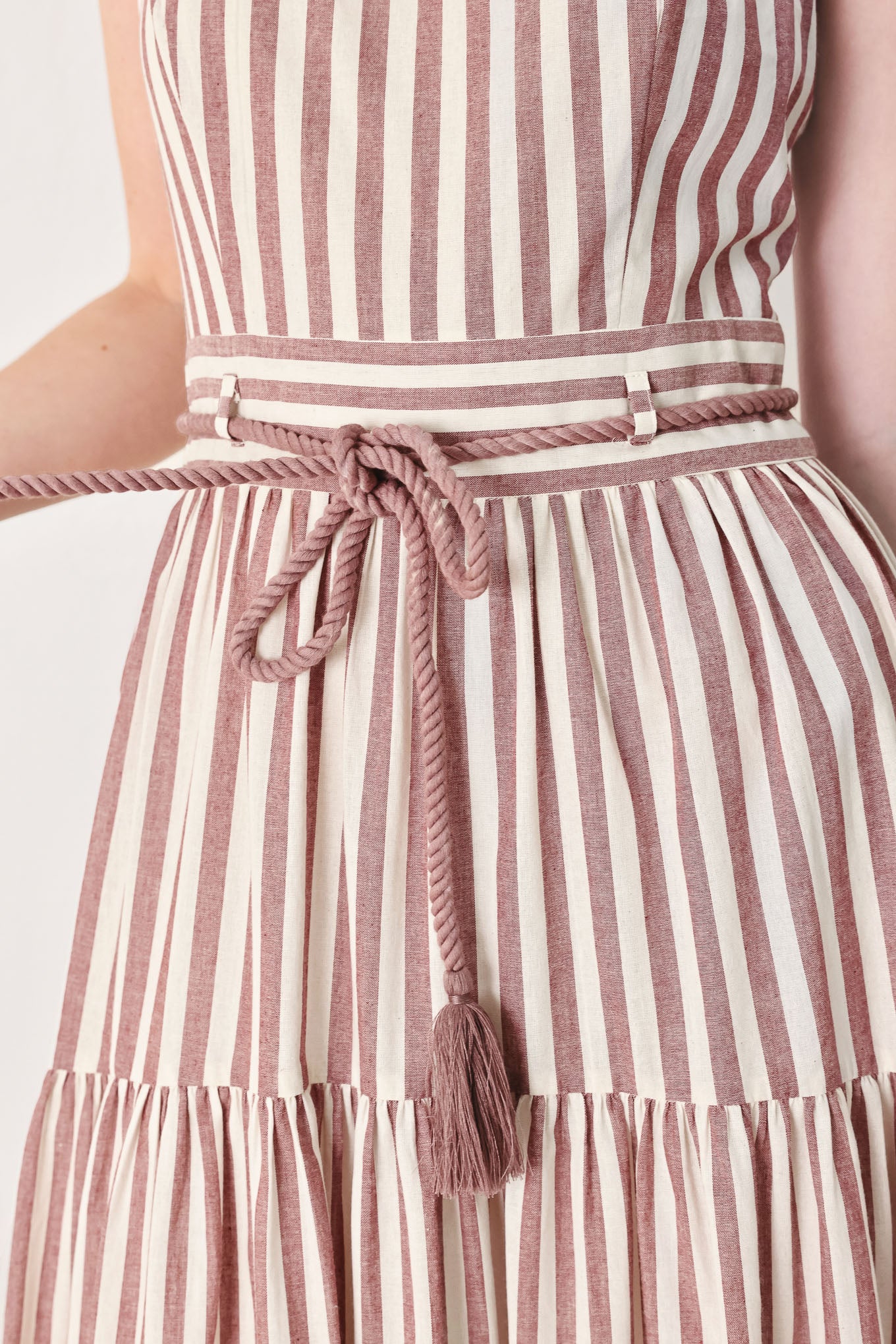 Close up of a burgundy striped woven ankle dress featuring straight neckline, straps, rope tie, tier skirt and back zipper closure | FREEMARKET