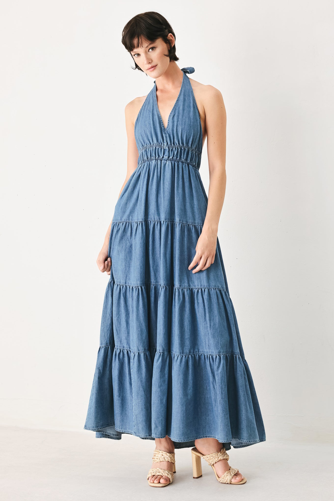 Woman wearing a blue denim midi dress featuring halter neckline, elastic waist, tier skirt, and bare back with tie | FREEMARKET