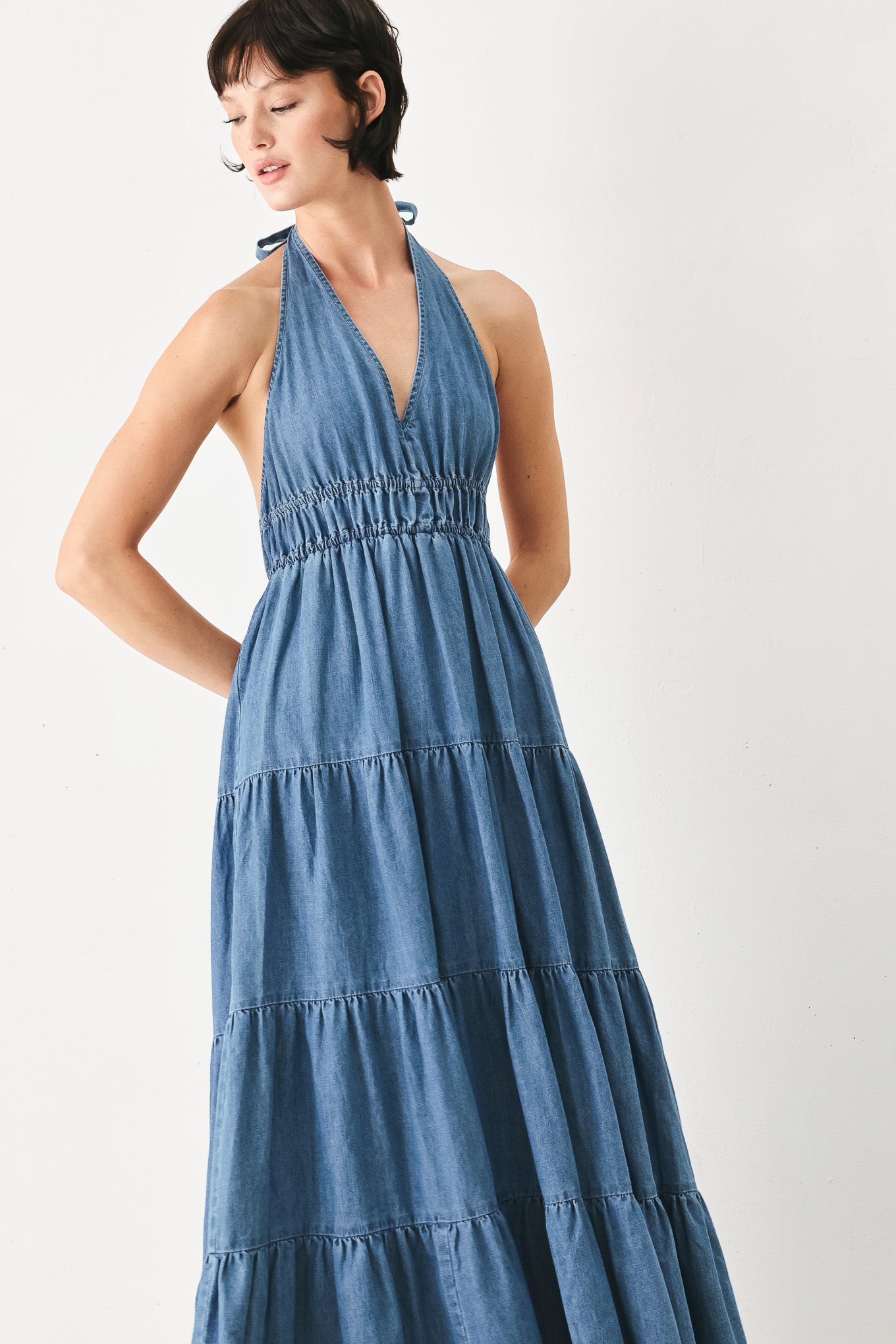 Woman wearing a blue denim midi dress featuring halter neckline, elastic waist, tier skirt, and bare back with tie | FREEMARKET