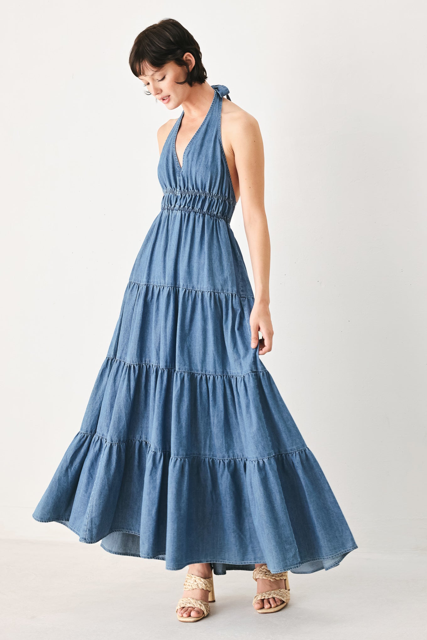 Woman wearing a blue denim midi dress featuring halter neckline, elastic waist, tier skirt, and bare back with tie | FREEMARKET