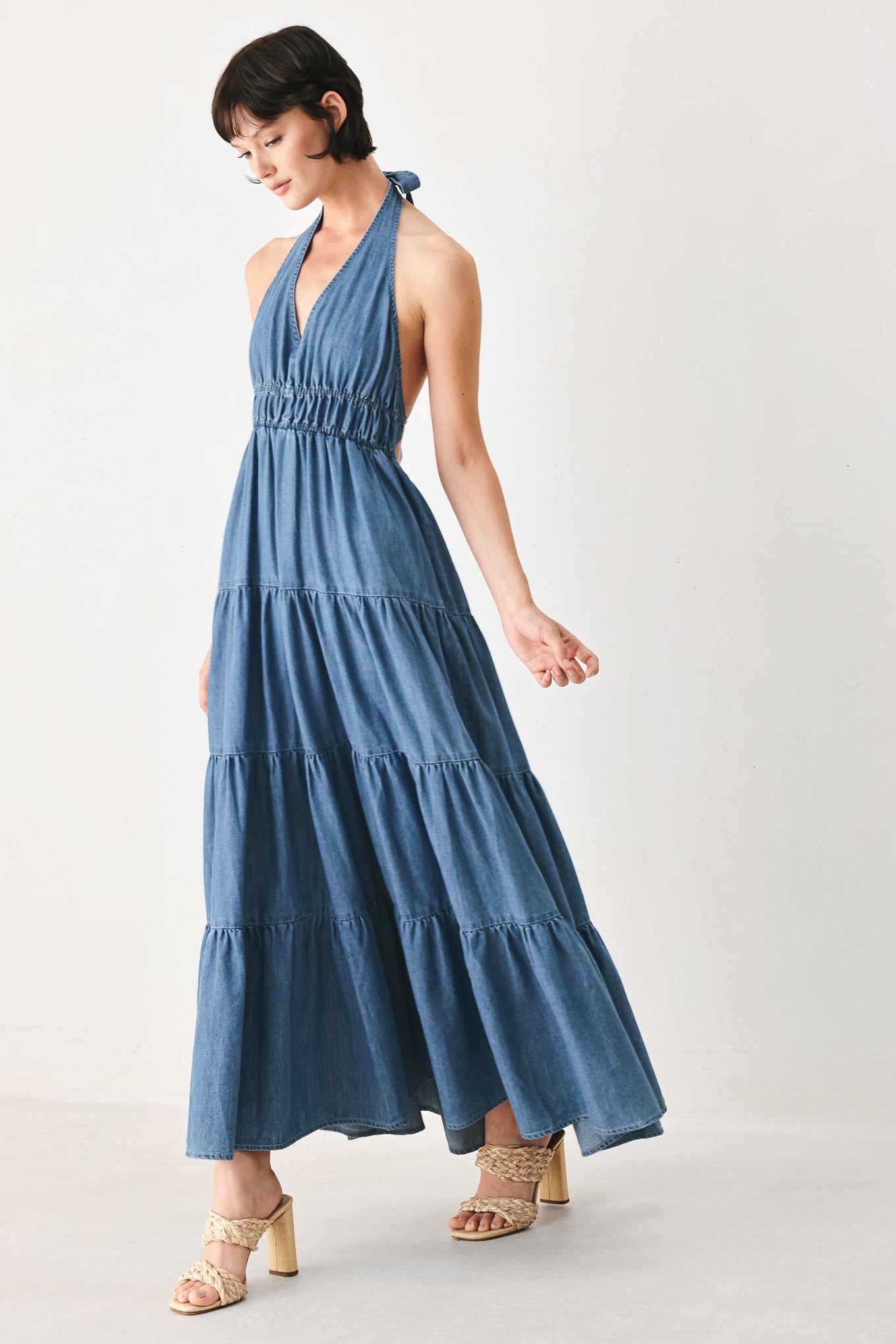 Woman wearing a blue denim midi dress featuring halter neckline, elastic waist, tier skirt, and bare back with tie | FREEMARKET
