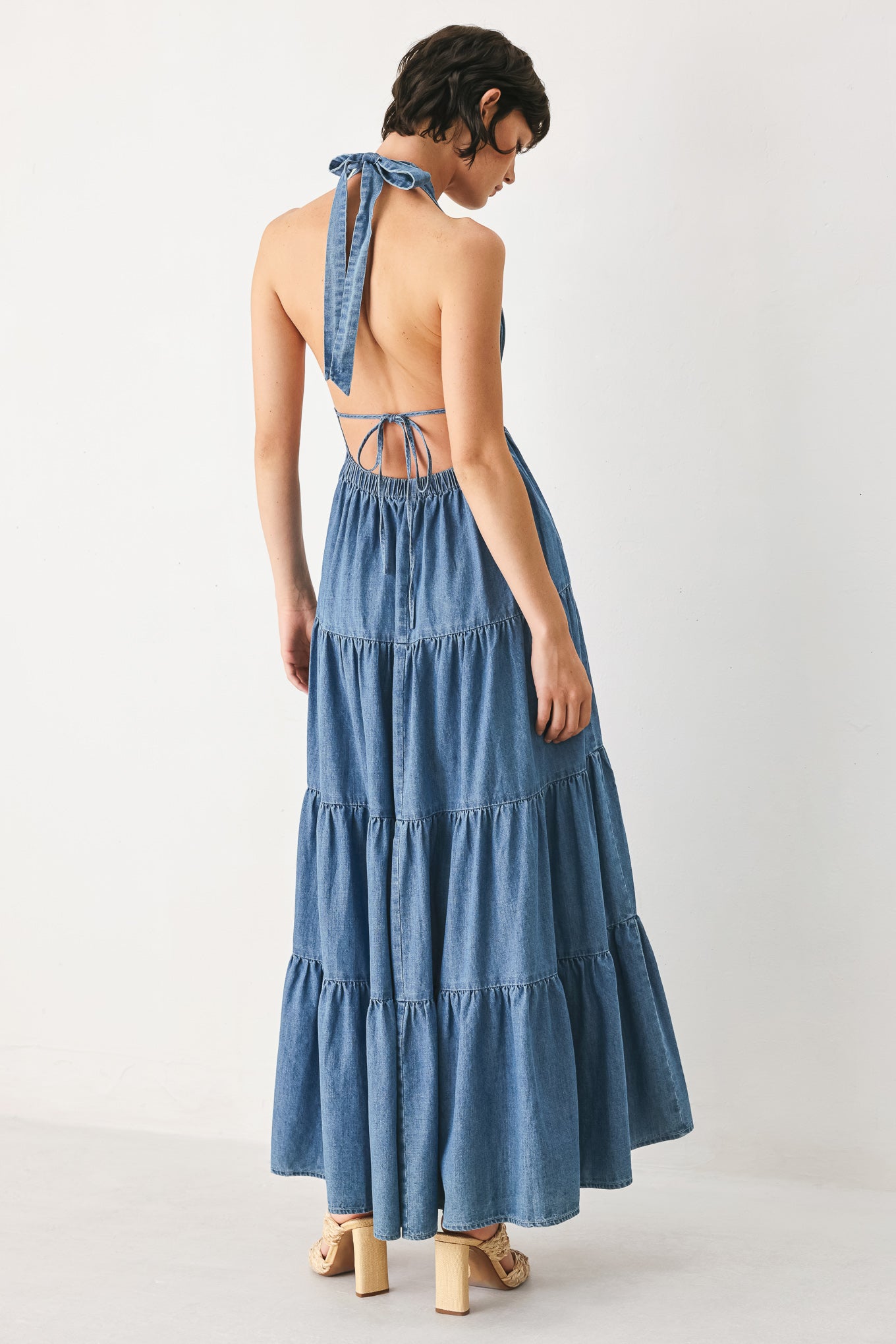 Woman wearing a blue denim midi dress featuring halter neckline, elastic waist, tier skirt, and bare back with tie | FREEMARKET