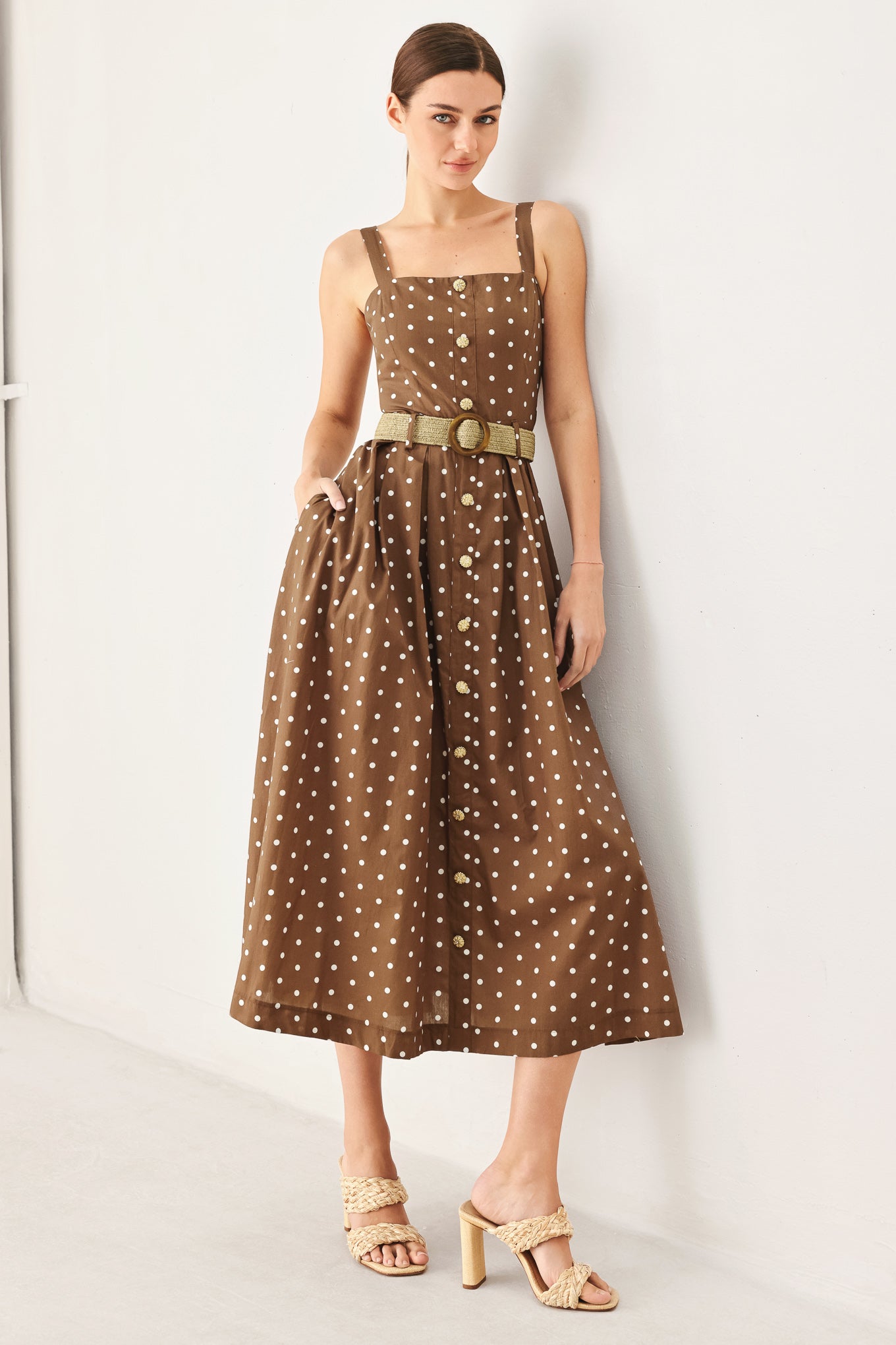 Woman wearing a brown polka dot dress with a belt against a white background