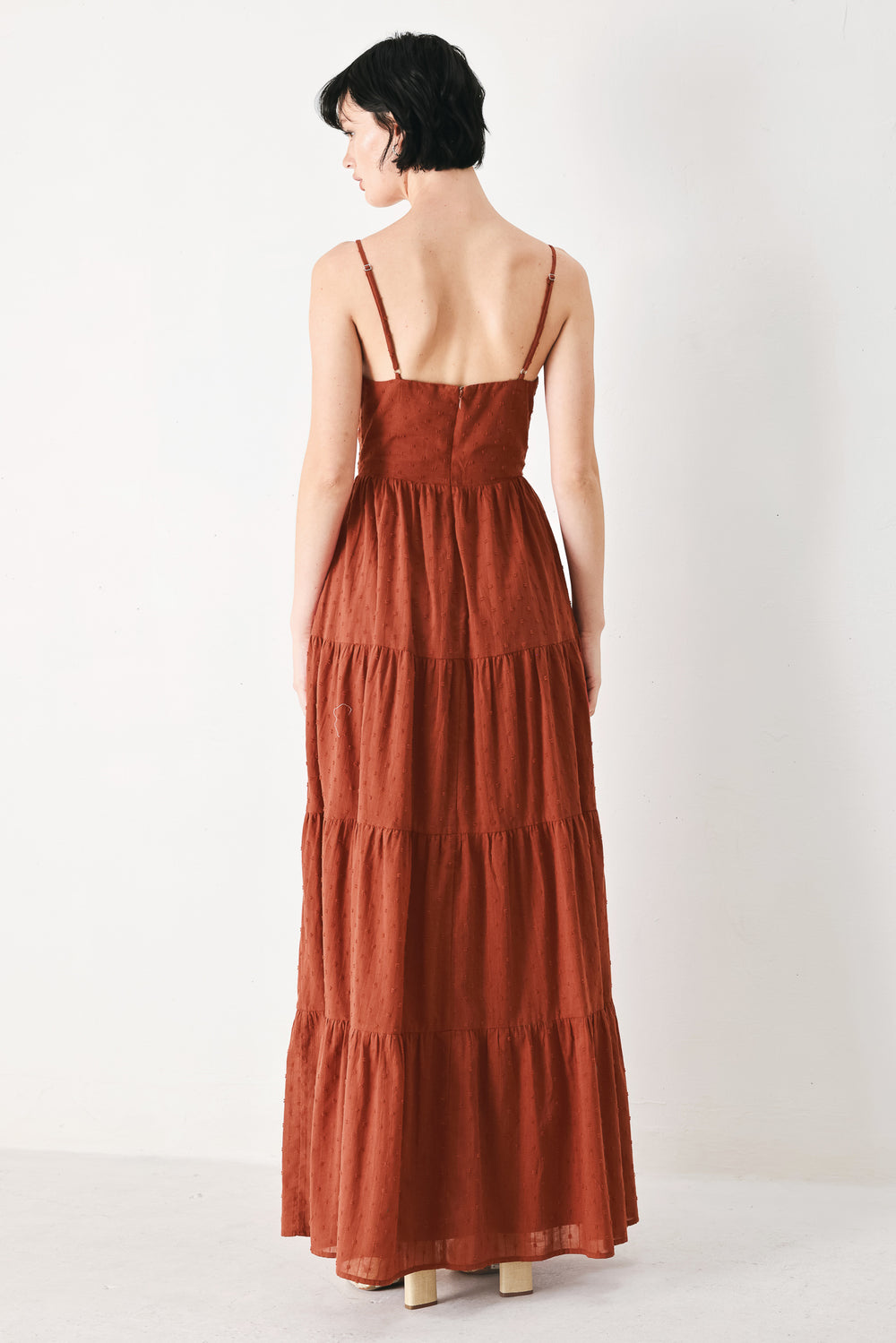 Woman wearing a rust solid textured woven maxi dress featuring cami top with front center cut out, straps, tier skirt and back zipper closure | FREEMARKET