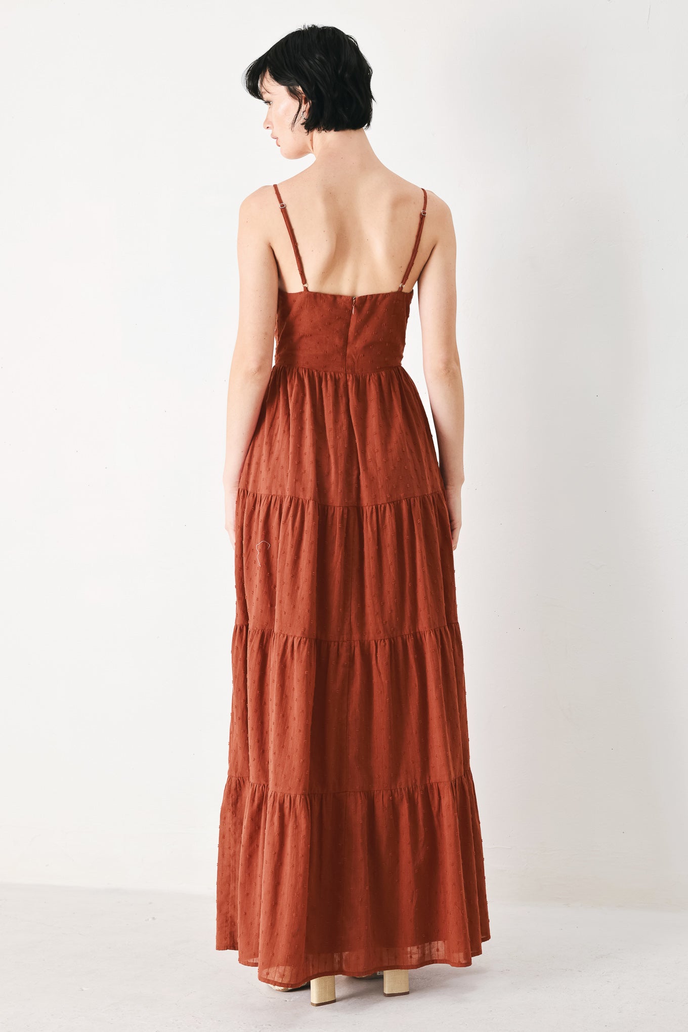 Woman wearing a rust solid textured woven maxi dress featuring cami top with front center cut out, straps, tier skirt and back zipper closure | FREEMARKET