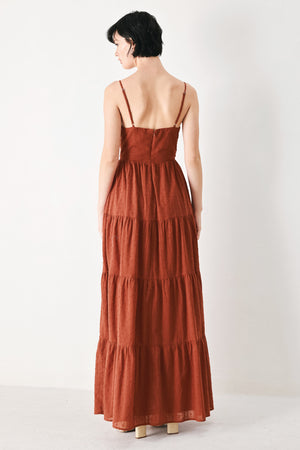Woman wearing a rust solid textured woven maxi dress featuring cami top with front center cut out, straps, tier skirt and back zipper closure | FREEMARKET