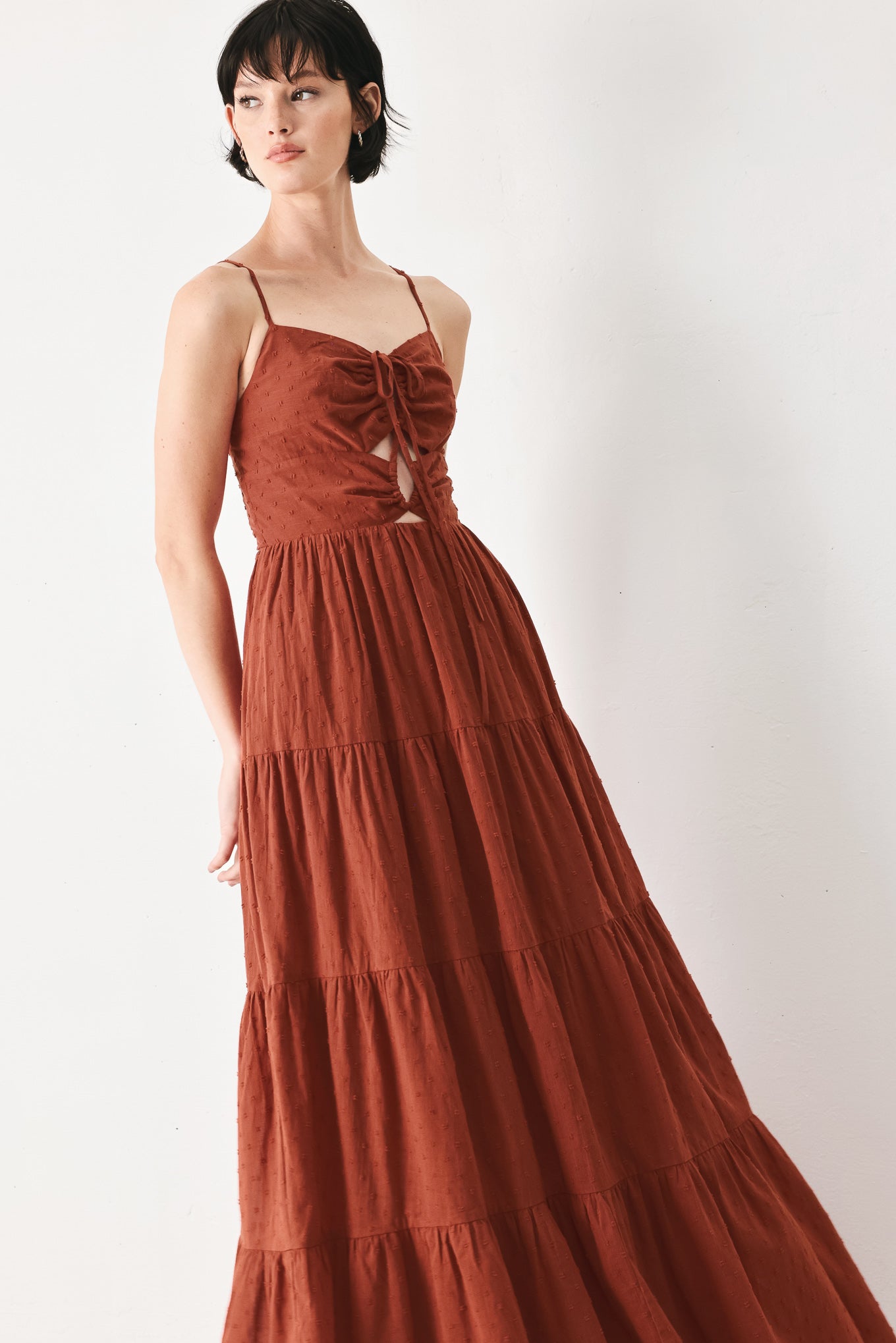 Woman wearing a rust solid textured woven maxi dress featuring cami top with front center cut out, straps, tier skirt and back zipper closure | FREEMARKET