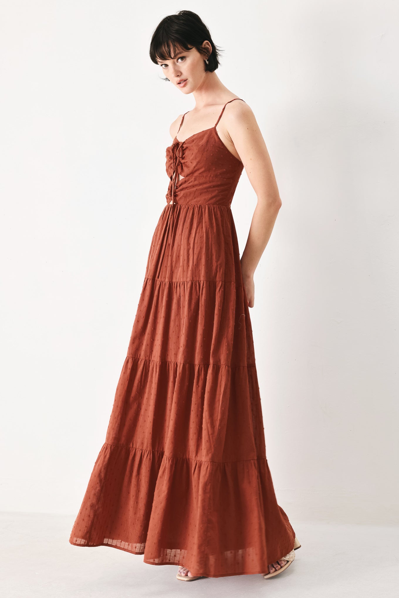 Woman wearing a rust solid textured woven maxi dress featuring cami top with front center cut out, straps, tier skirt and back zipper closure | FREEMARKET