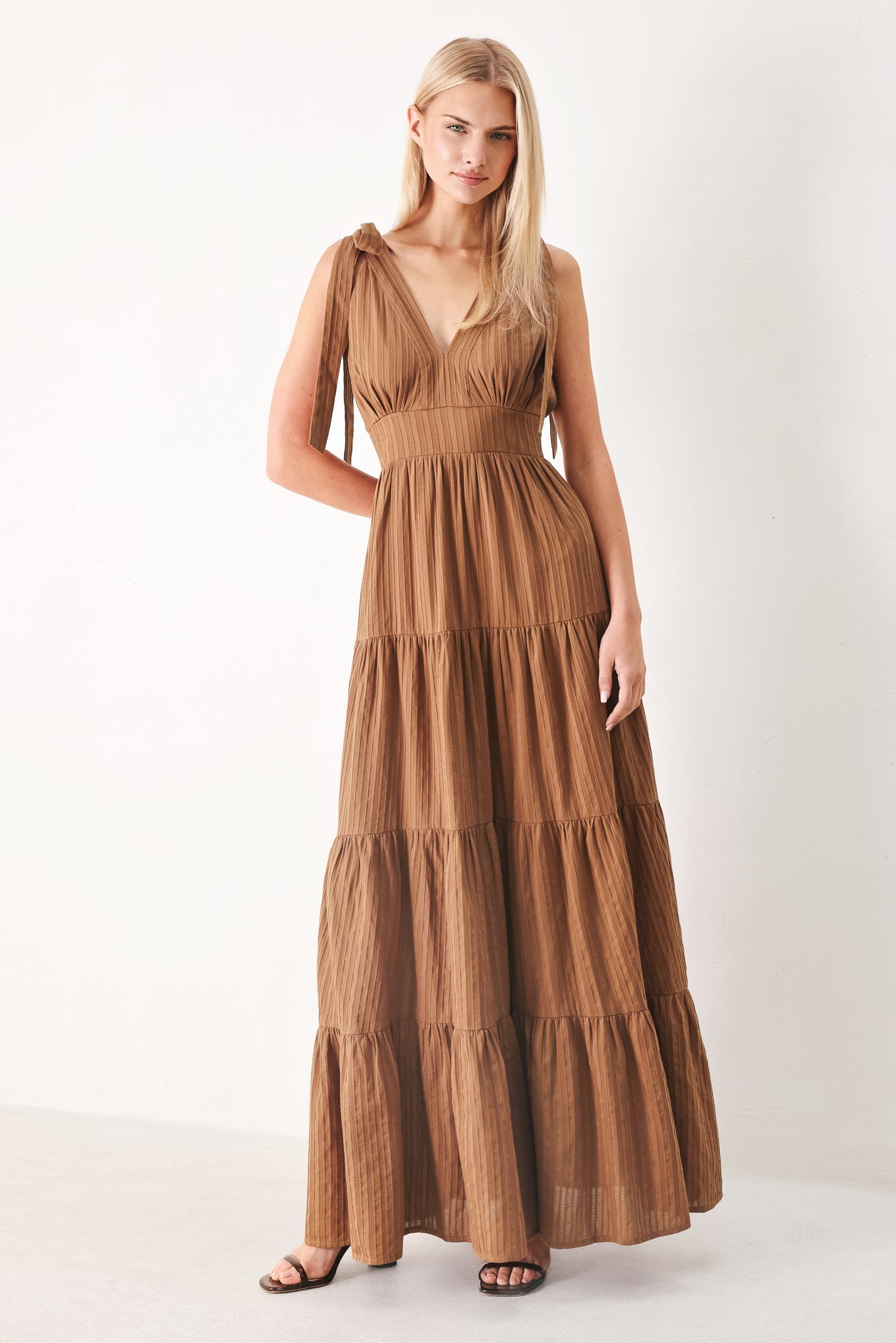 Woman wearing a brown tiered maxi dress featuring V neckline, shoulder ties, tier skirt and smocked back waistband | FREEMARKET