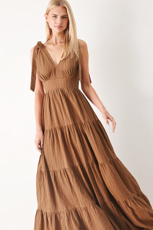 Woman wearing a brown tiered maxi dress featuring V neckline, shoulder ties, tier skirt and smocked back waistband | FREEMARKET