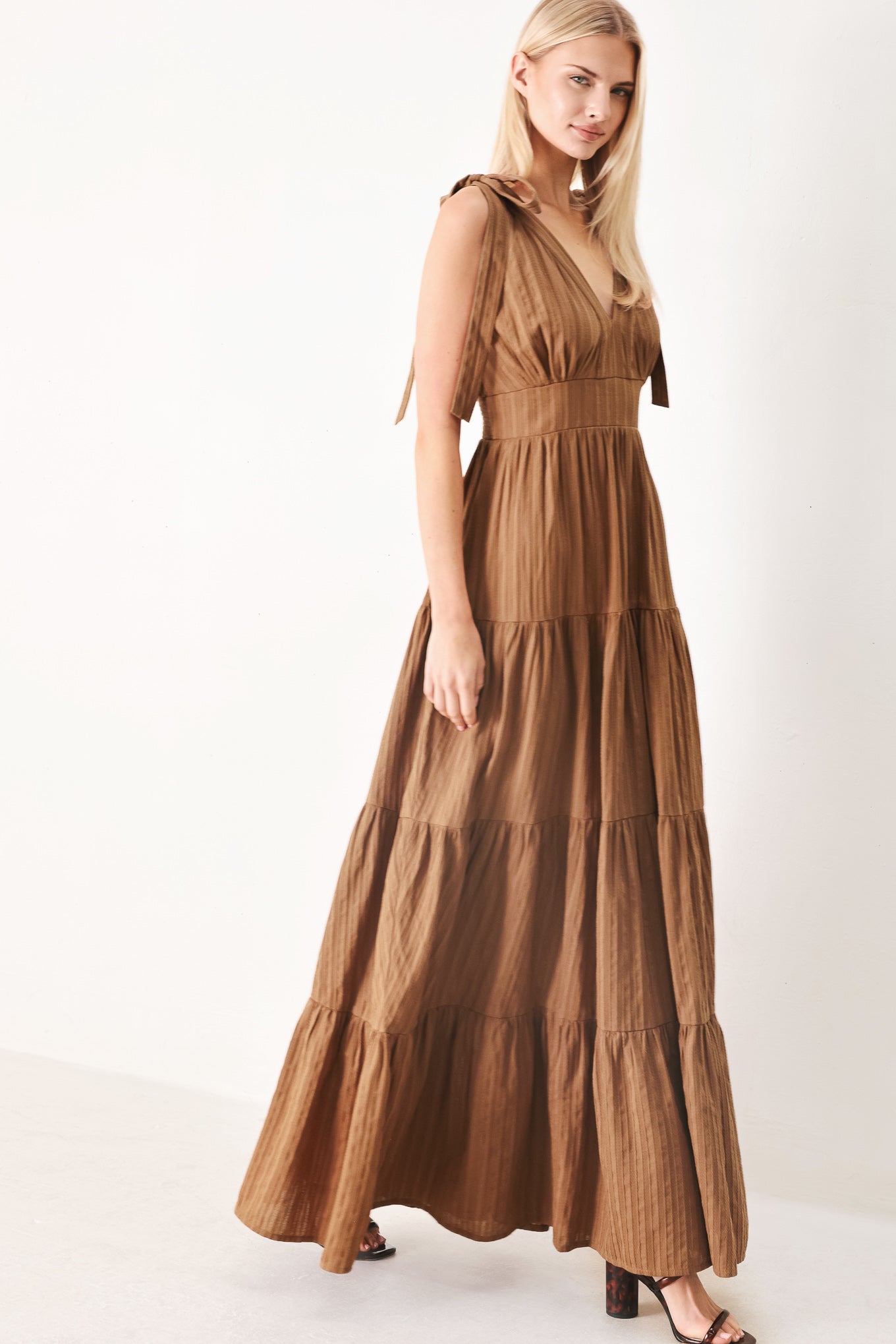 Woman wearing a brown tiered maxi dress featuring V neckline, shoulder ties, tier skirt and smocked back waistband | FREEMARKET
