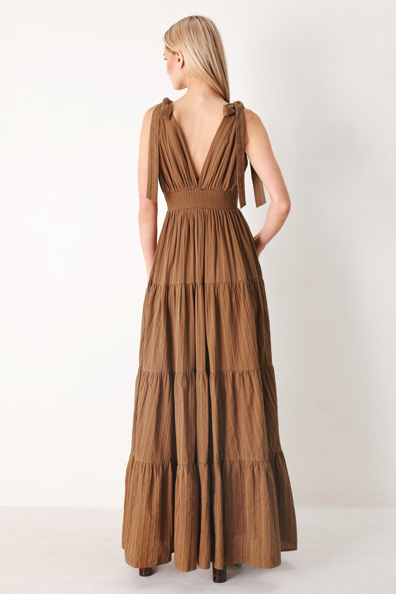 Woman wearing a brown tiered maxi dress featuring V neckline, shoulder ties, tier skirt and smocked back waistband | FREEMARKET