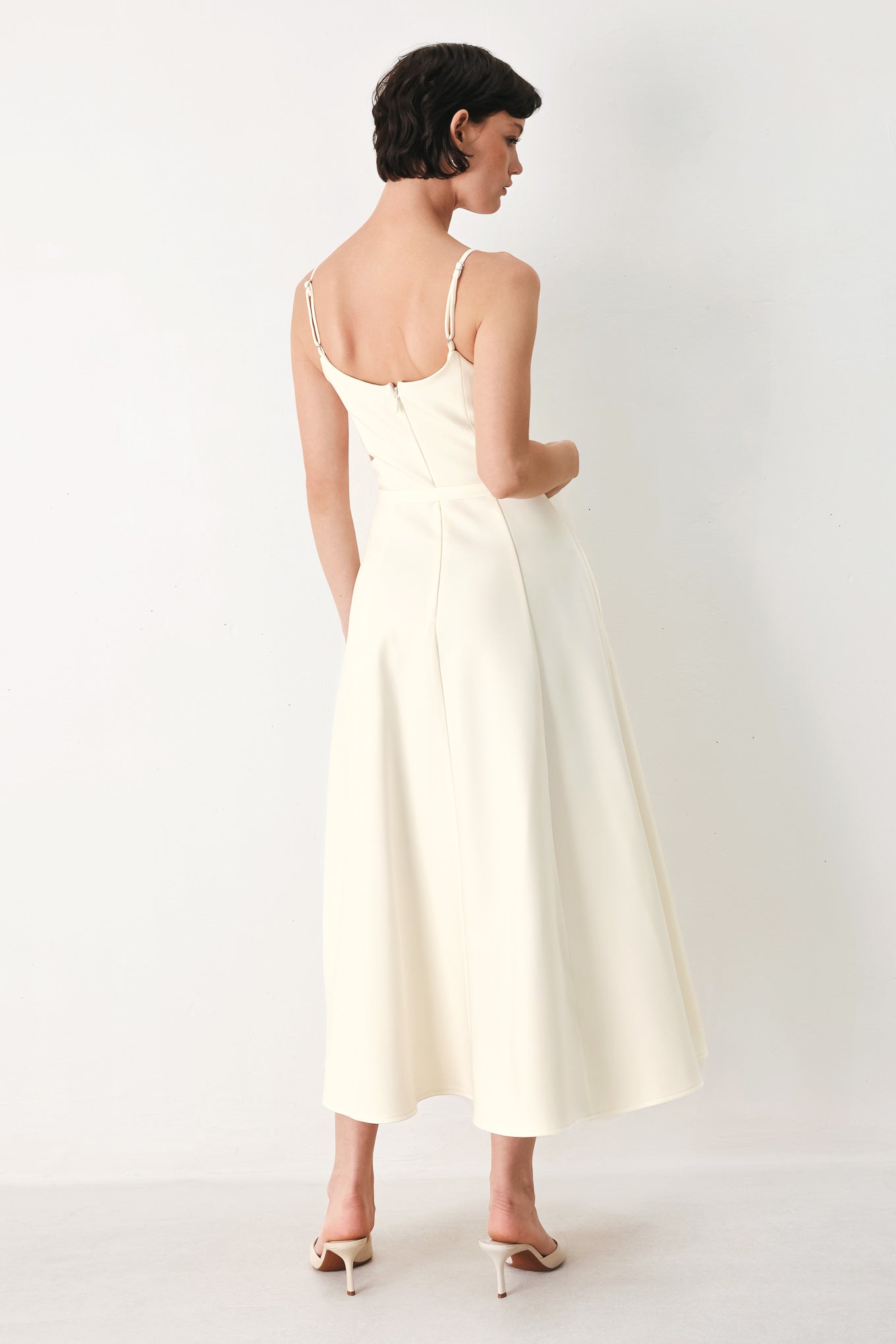 Woman wearing an ivory midi dress with cut-out design featuring cam top, cut out at waistline, self belt, circle skirt and back zipper closure | FREEMARKET