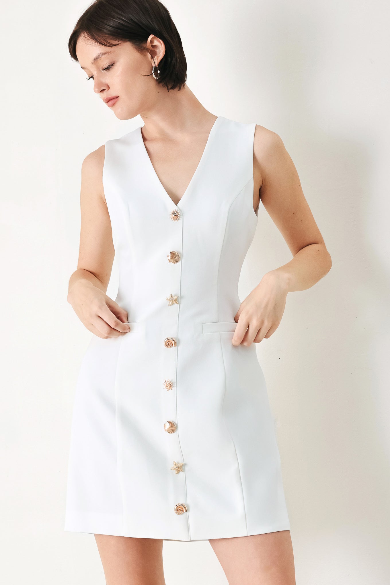 A solid woven mini dress featuring V neckline, sleeveless, button detail and back zipper closure
