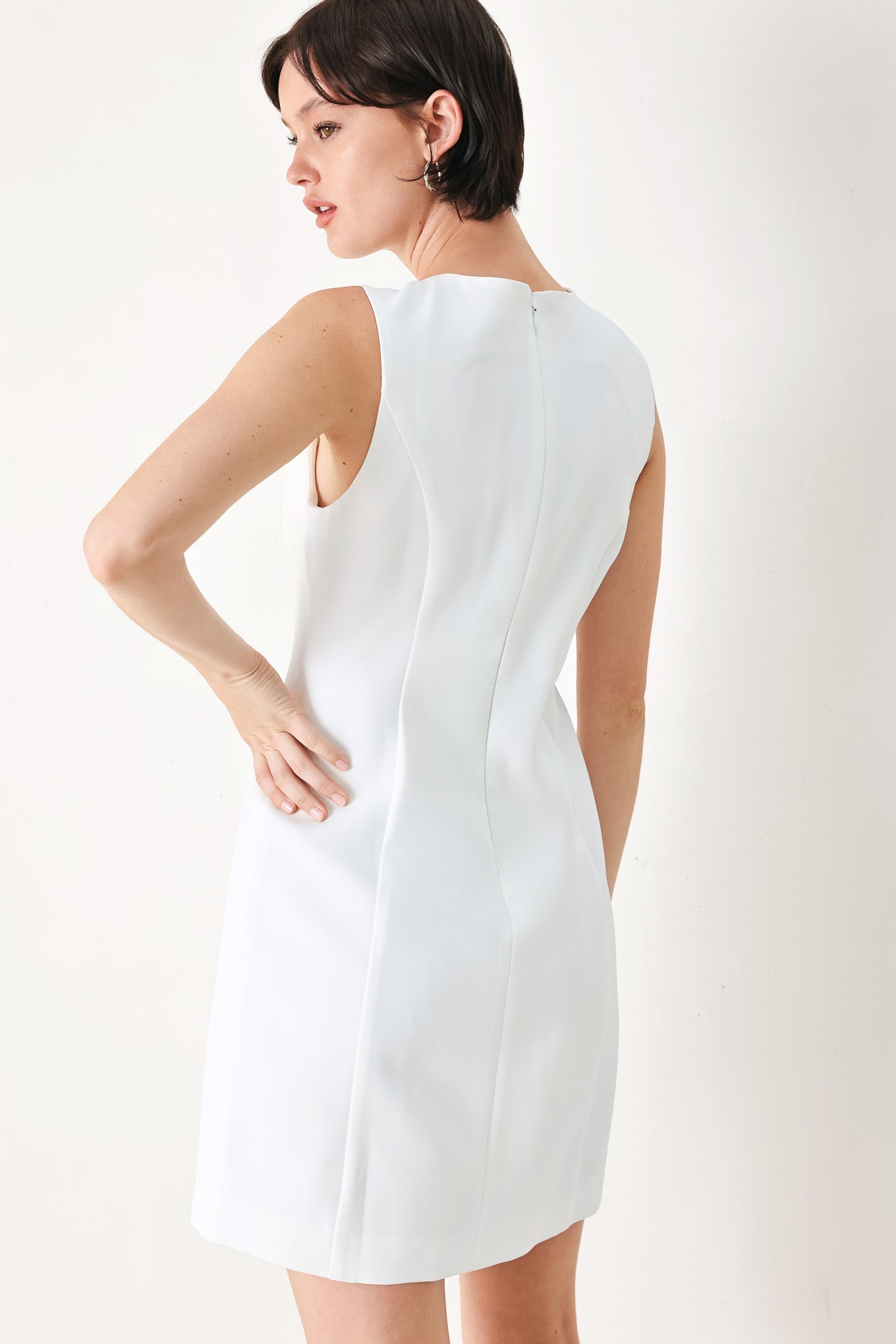 A solid woven mini dress featuring V neckline, sleeveless, button detail and back zipper closure