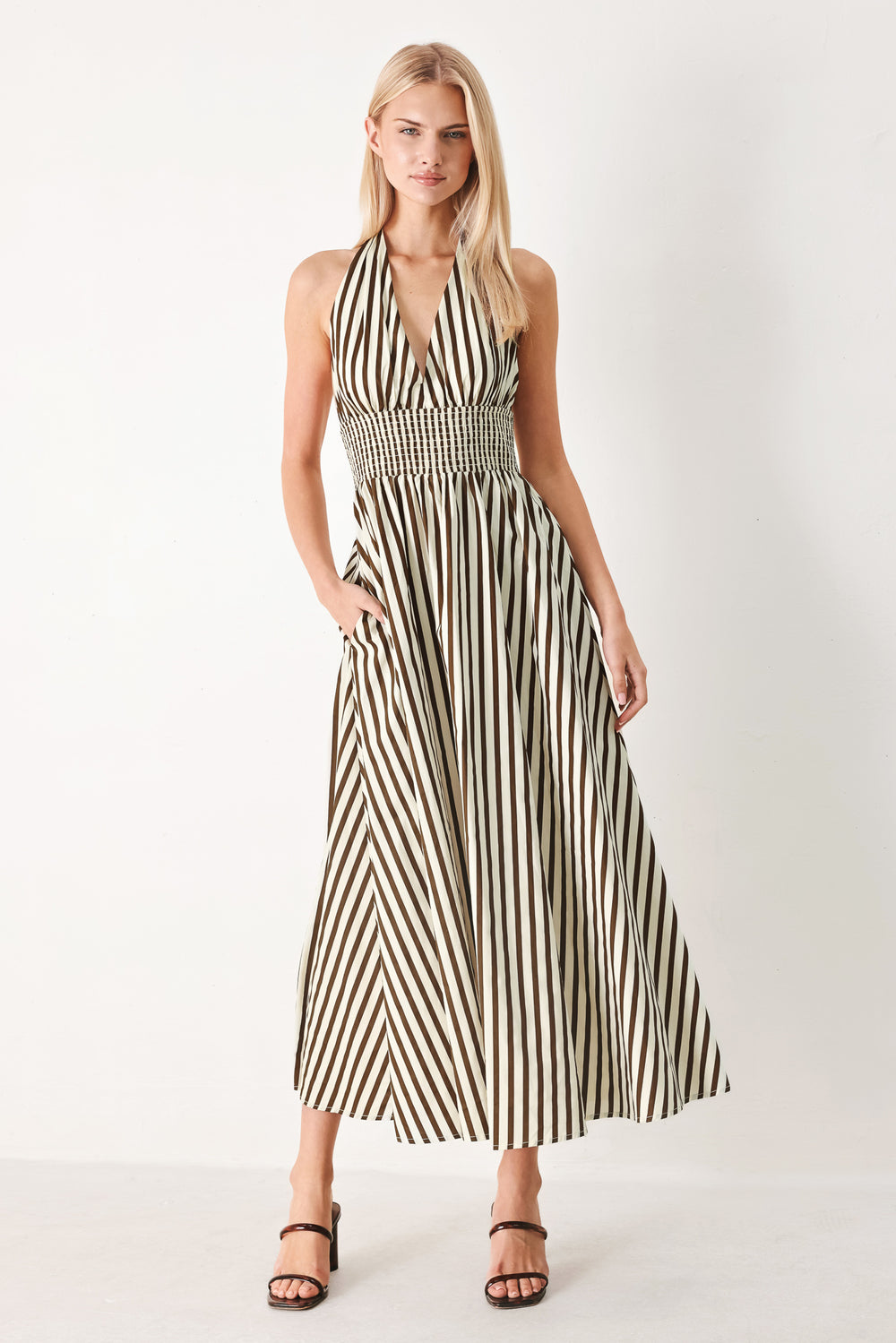 Woman wearing a black and white striped woven midi dress featuring halter neckline with back neck tie, full skirt, pockets and bare back with smocked back waist band | FREEMARKET