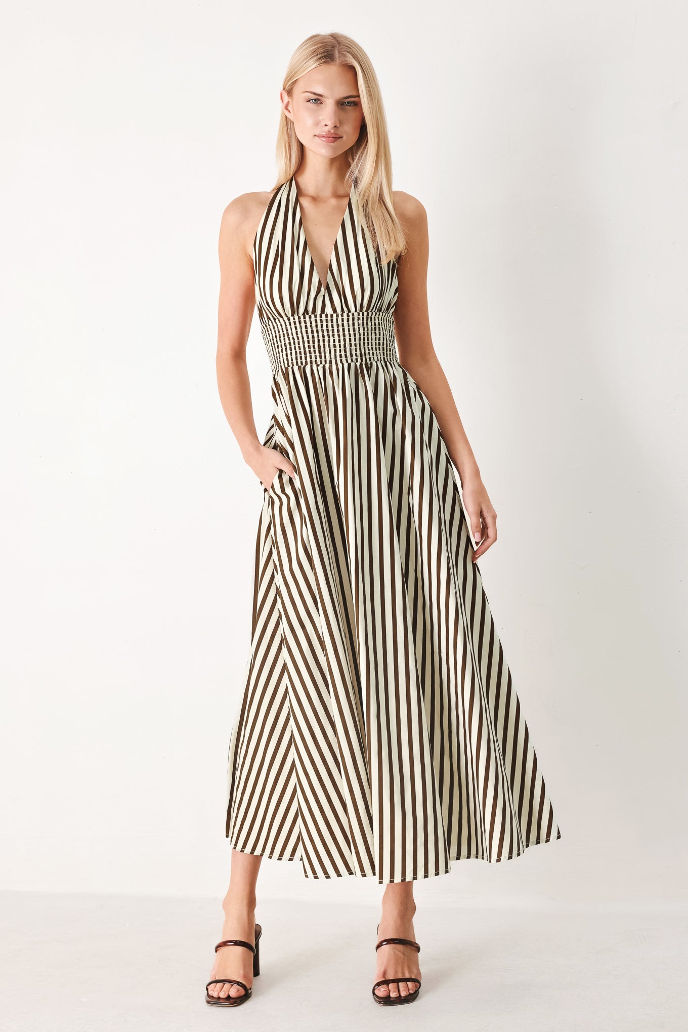 Woman wearing a black and white striped woven midi dress featuring halter neckline with back neck tie, full skirt, pockets and bare back with smocked back waist band | FREEMARKET