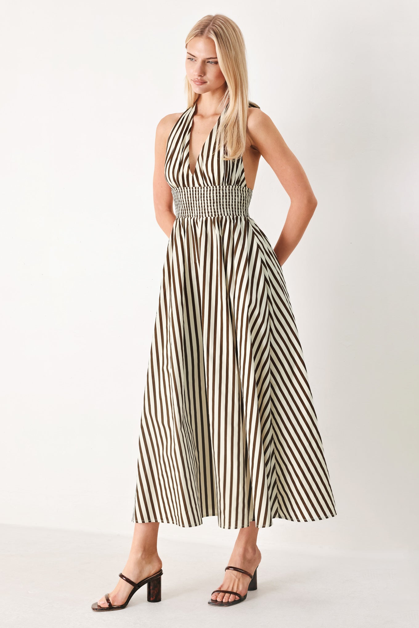 Woman wearing a black and white striped woven midi dress featuring halter neckline with back neck tie, full skirt, pockets and bare back with smocked back waist band | FREEMARKET
