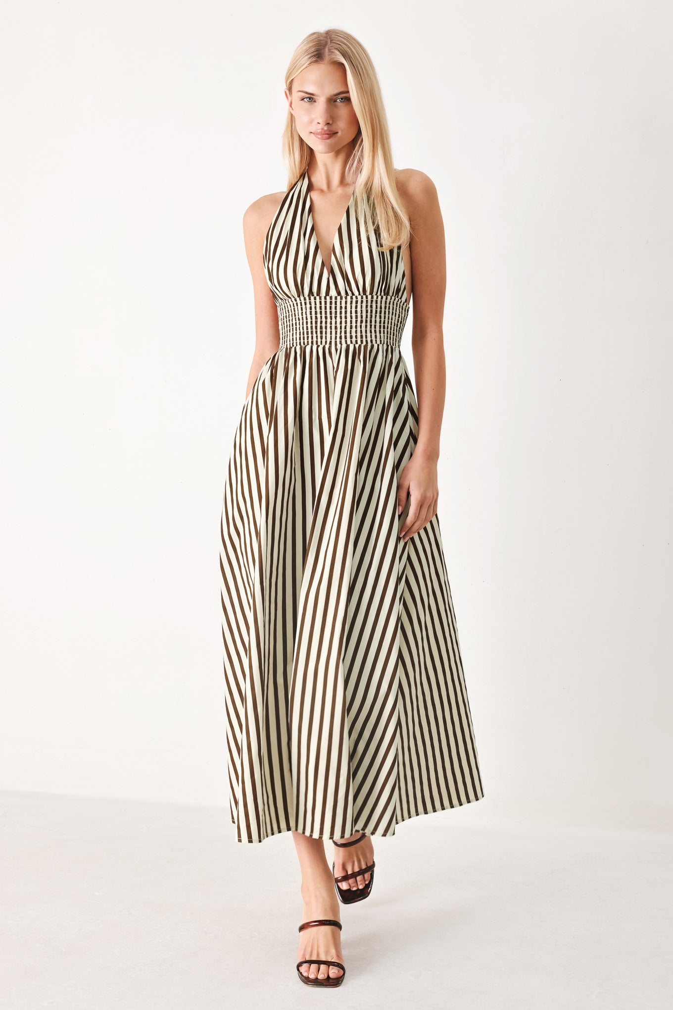 Woman wearing a black and white striped woven midi dress featuring halter neckline with back neck tie, full skirt, pockets and bare back with smocked back waist band | FREEMARKET