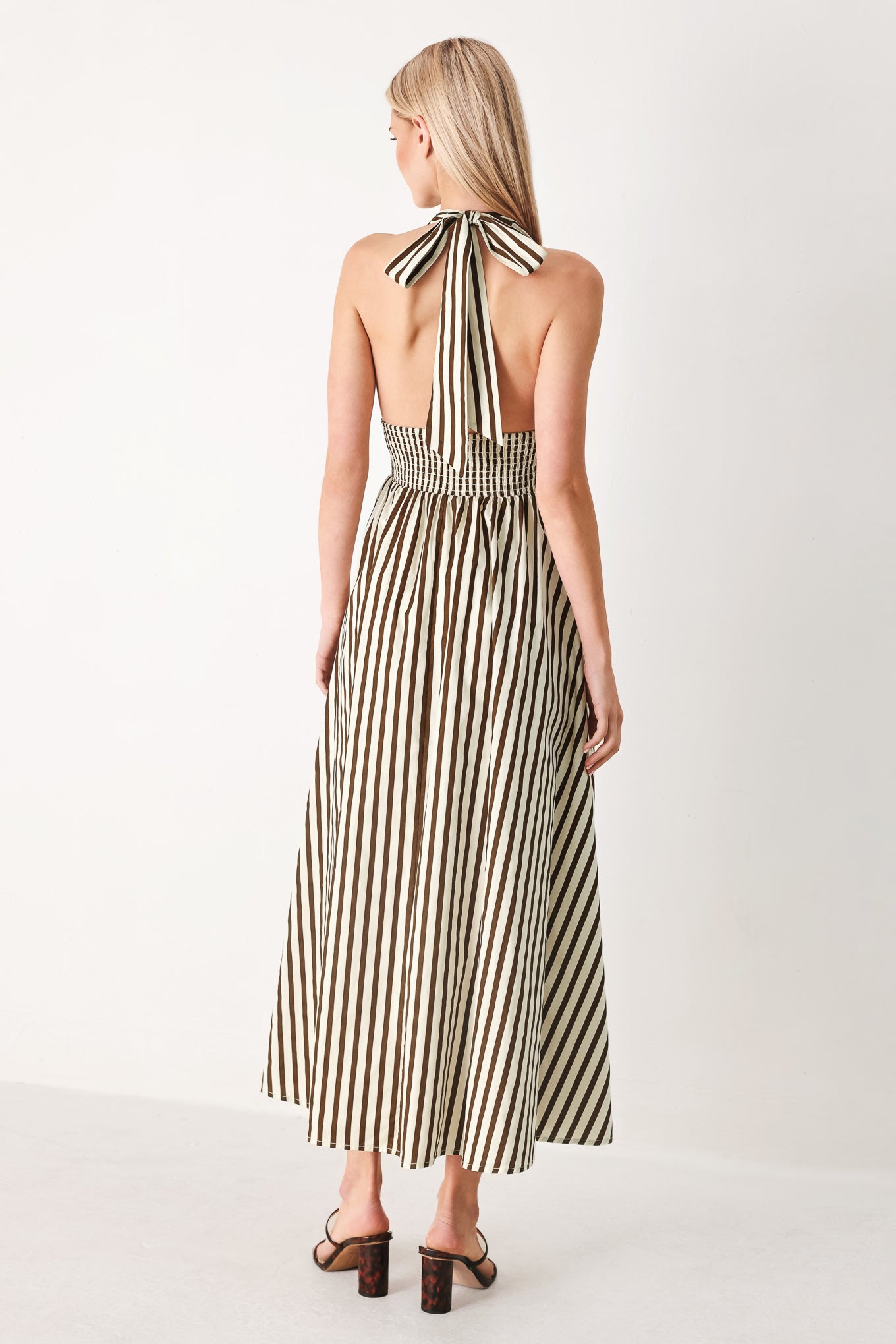 Woman wearing a black and white striped woven midi dress featuring halter neckline with back neck tie, full skirt, pockets and bare back with smocked back waist band | FREEMARKET