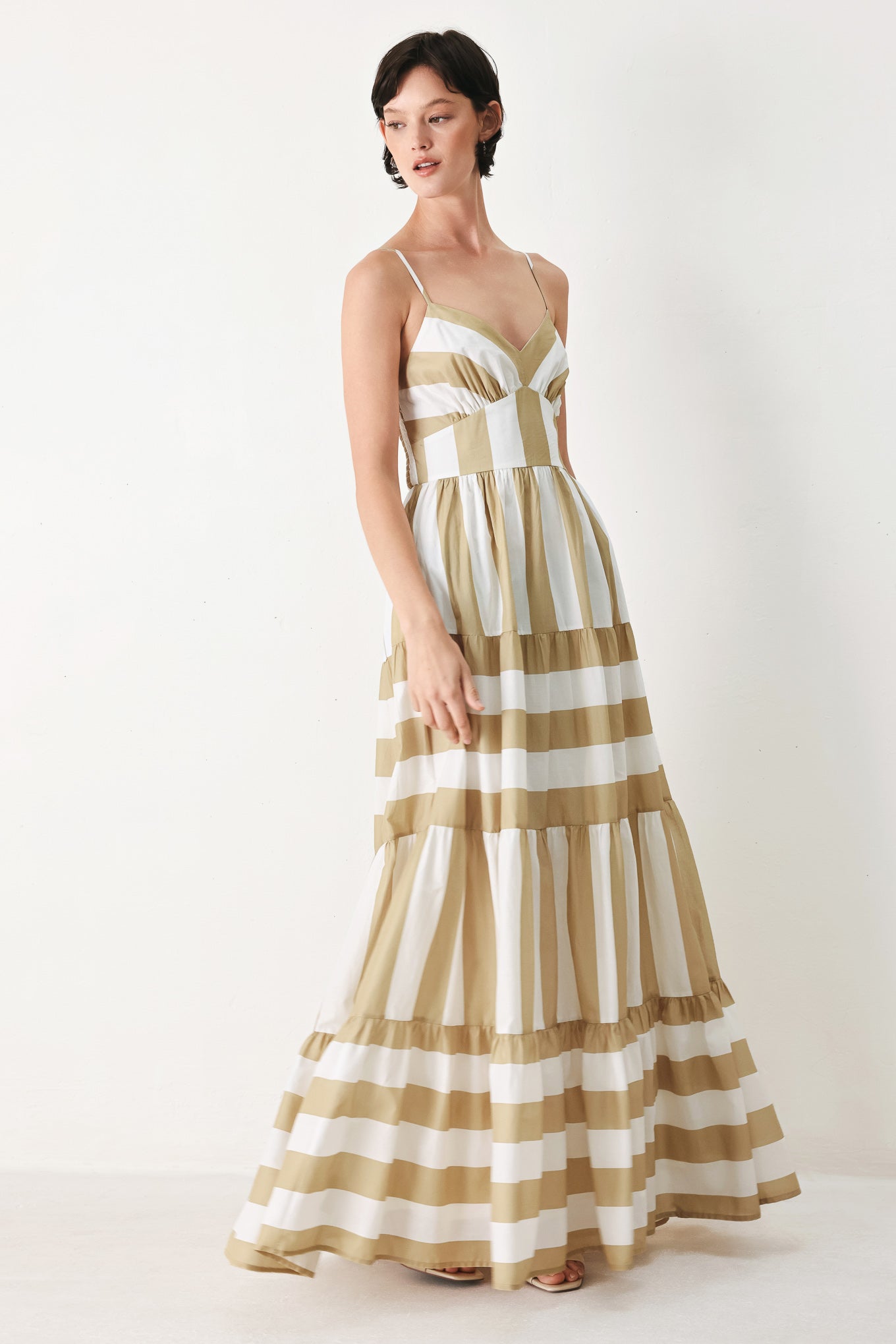 Woman wearing a taupe and white striped maxi dress featuring cami top, waist yoke, tier skirt and smocked back bodice | FREEMARKET