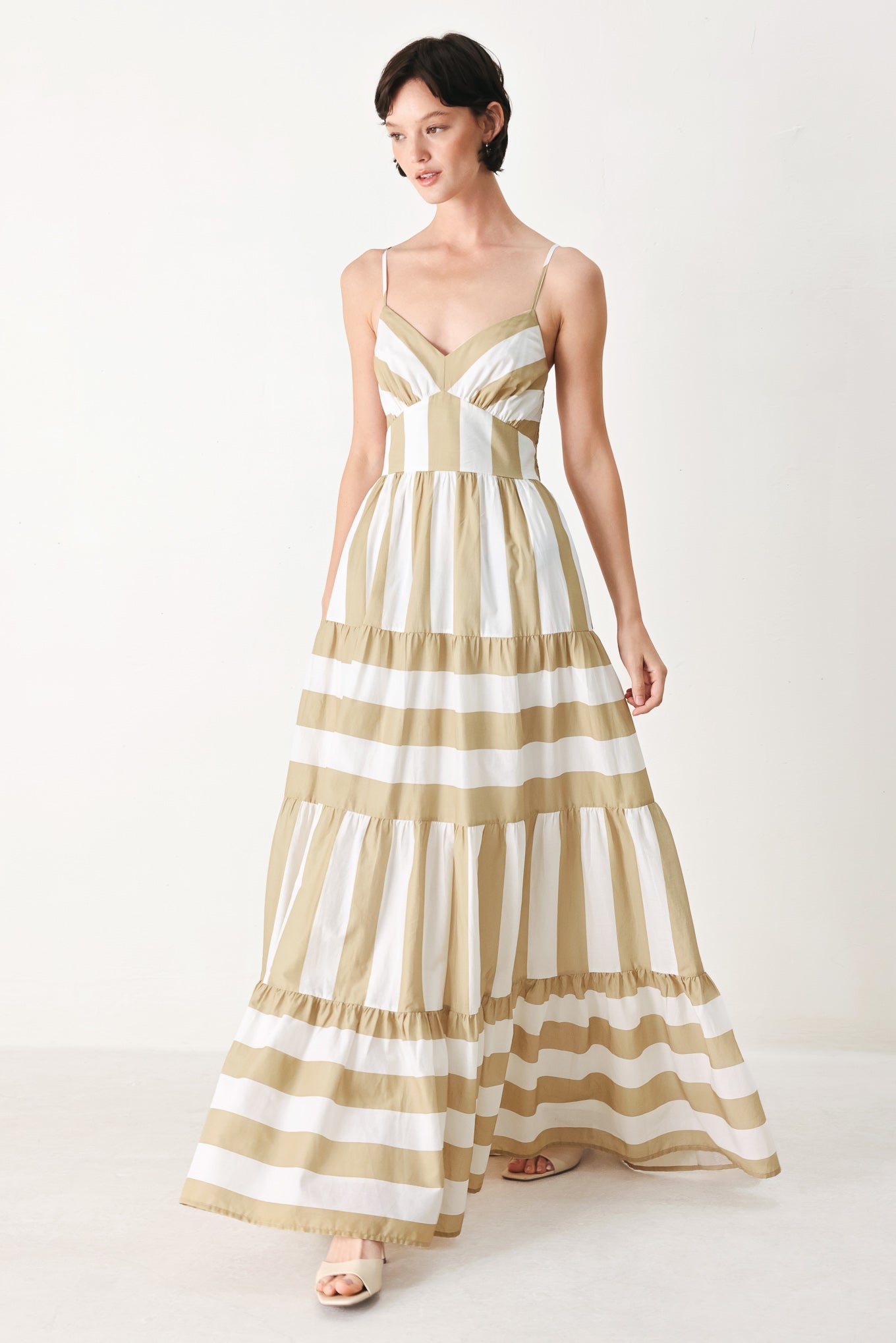 Woman wearing a taupe and white striped maxi dress featuring cami top, waist yoke, tier skirt and smocked back bodice | FREEMARKET