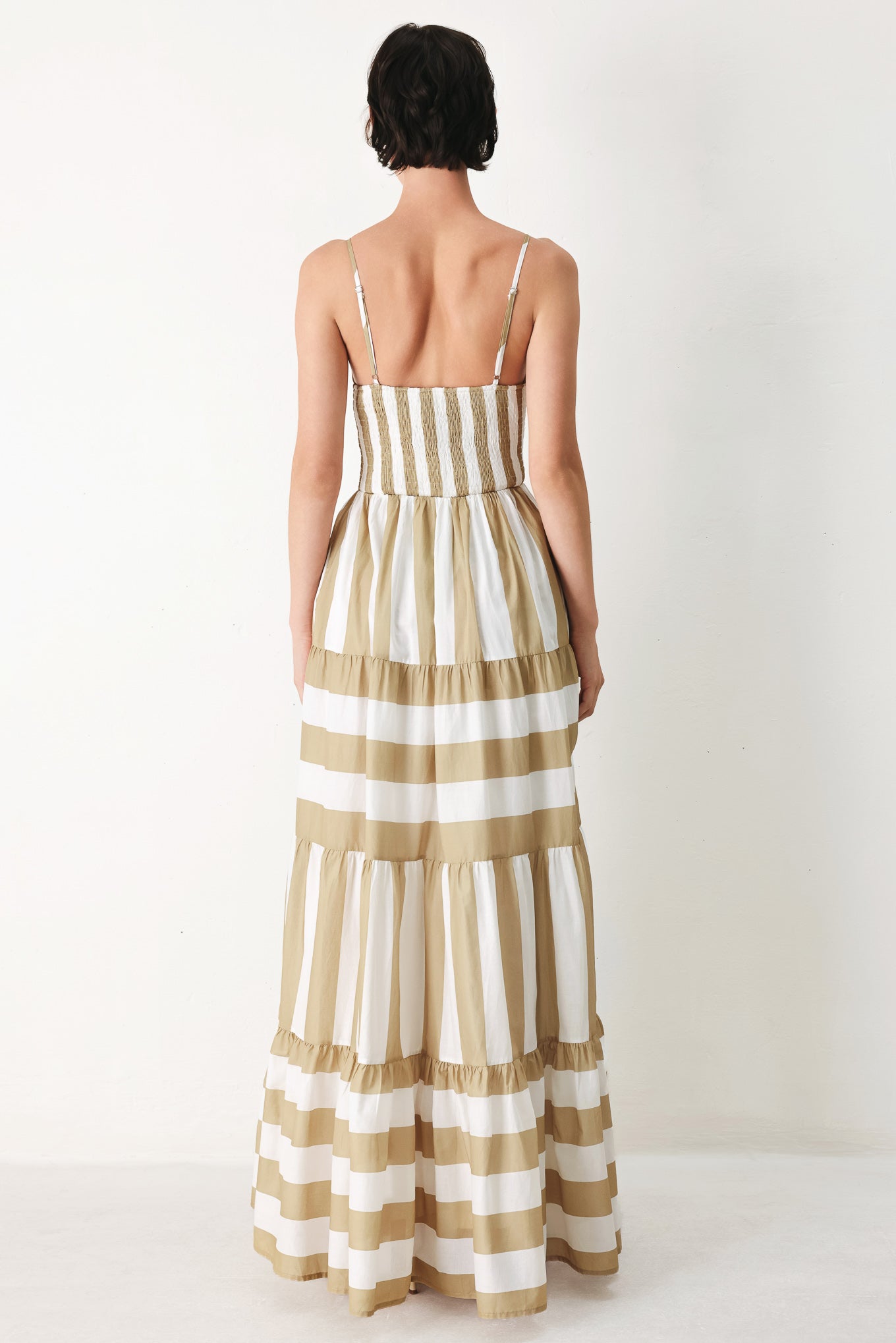 Woman wearing a taupe and white striped maxi dress featuring cami top, waist yoke, tier skirt and smocked back bodice | FREEMARKET