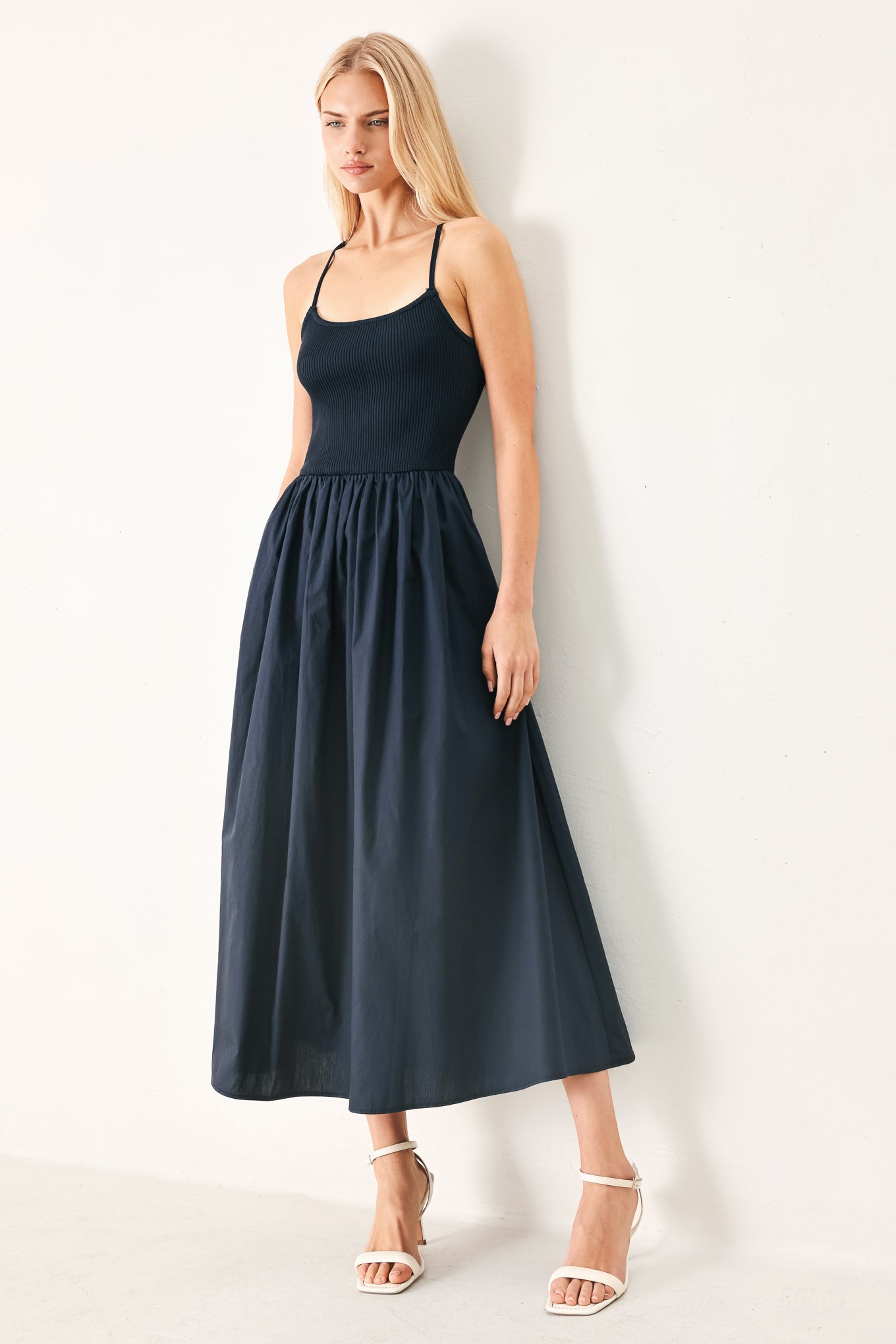 Woman wearing a navy sleeveless  midi dress featuring ribbed sweater knit tank top, solid woven skirt, bare back with lace up tie detail | FREEMARKET