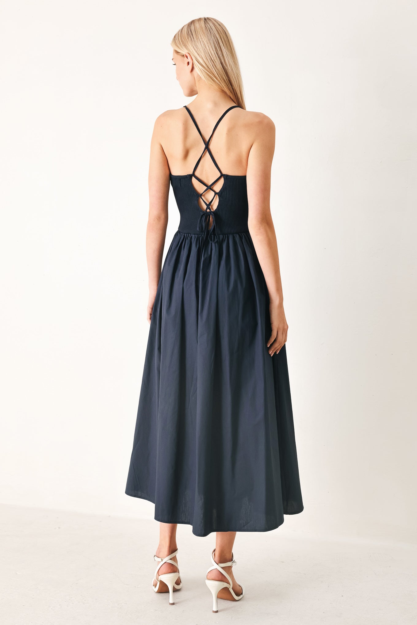 Woman wearing a navy sleeveless  midi dress featuring ribbed sweater knit tank top, solid woven skirt, bare back with lace up tie detail | FREEMARKET