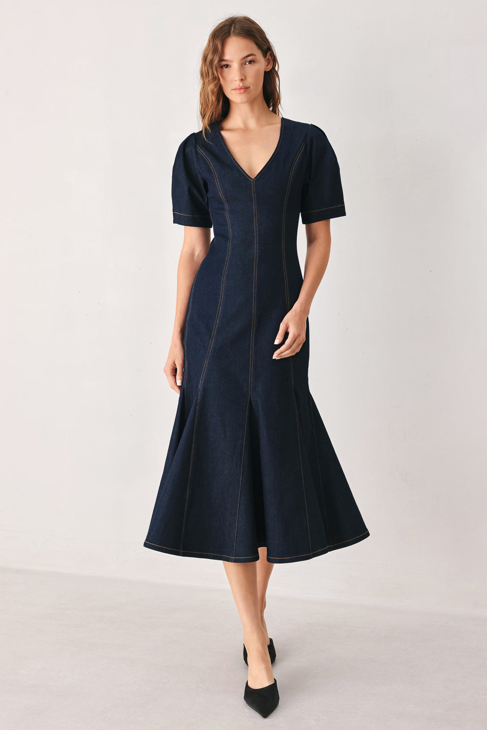 A woman wearing a dark navy blue denim midi dress with short puff sleeves, a V-neckline, and a flared skirt | FREEMARKET