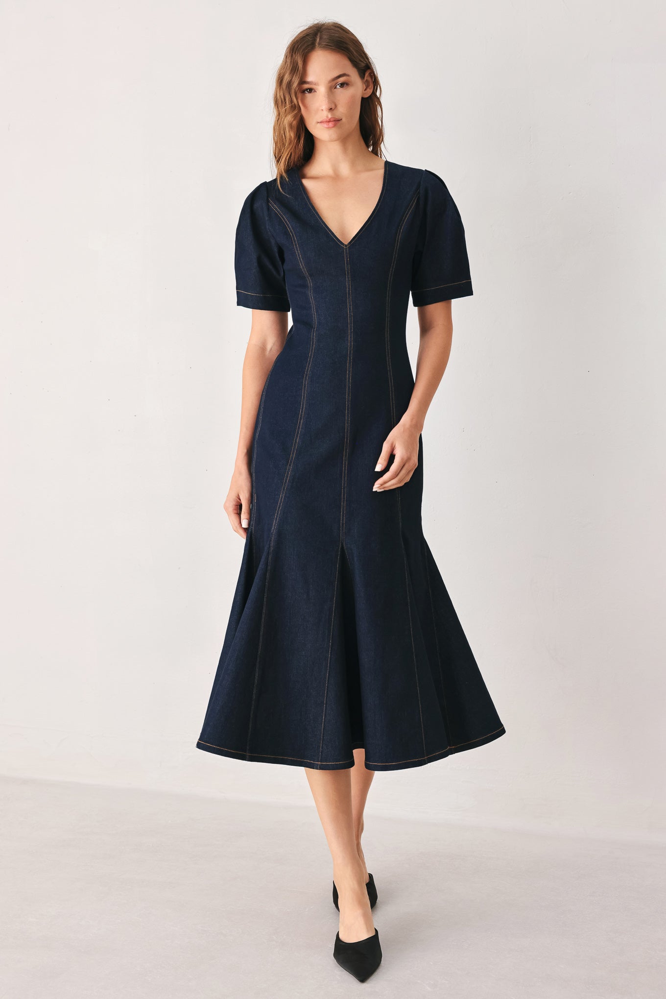 A woman wearing a dark navy blue denim midi dress with short puff sleeves, a V-neckline, and a flared skirt | FREEMARKET