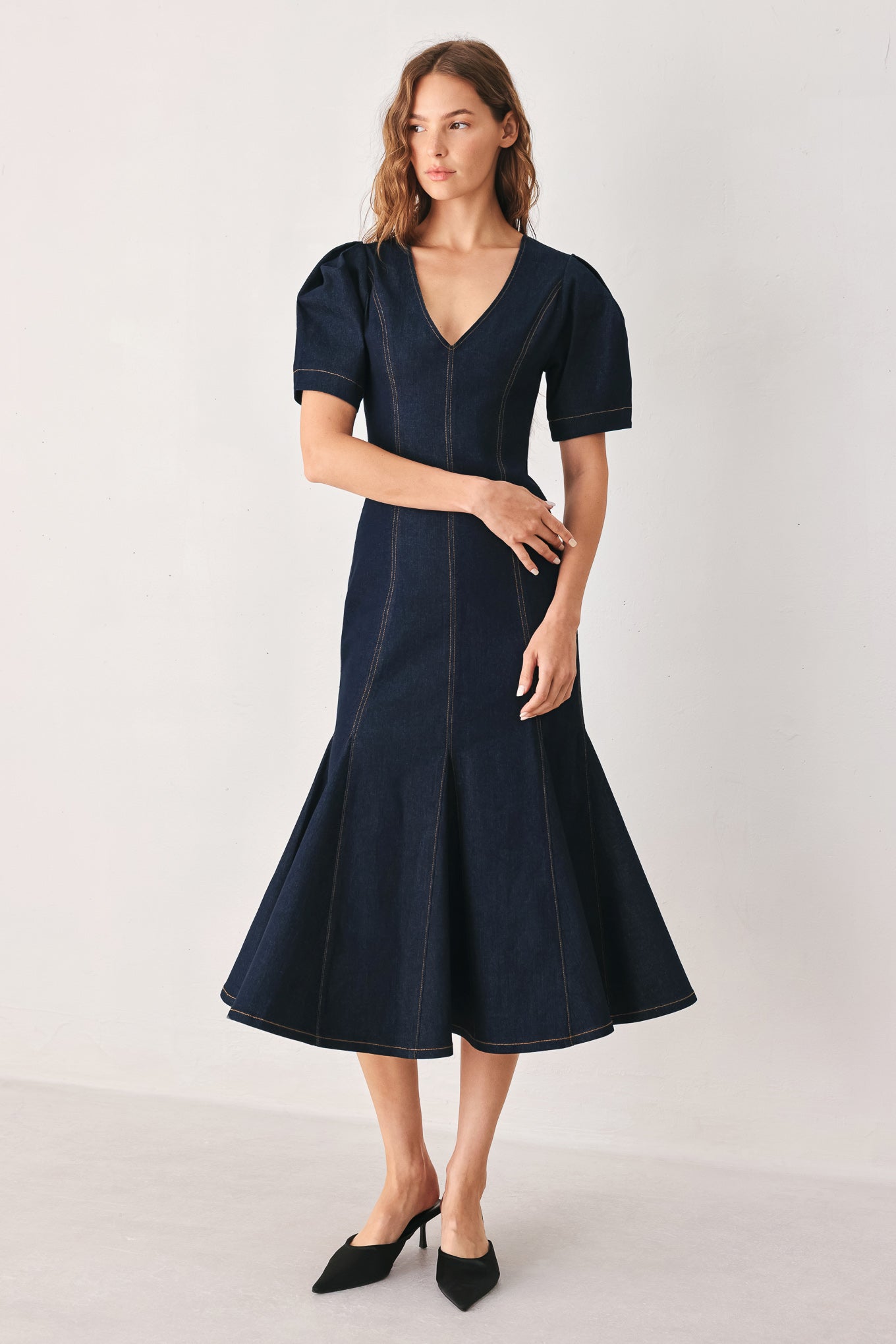 A woman wearing a dark navy blue denim midi dress with short puff sleeves, a V-neckline, and a flared skirt | FREEMARKET