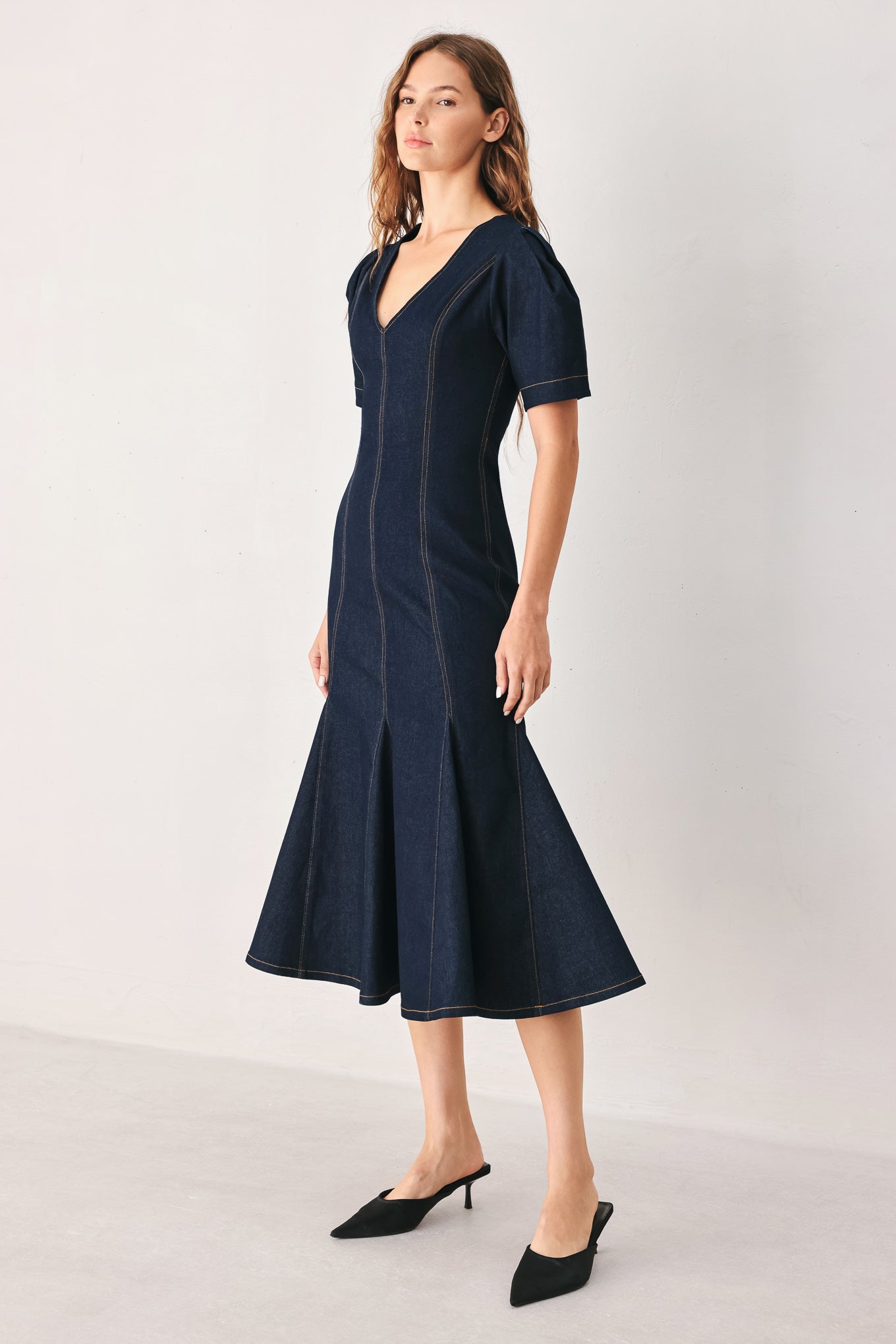 A woman wearing a dark navy blue denim midi dress with short puff sleeves, a V-neckline, and a flared skirt | FREEMARKET