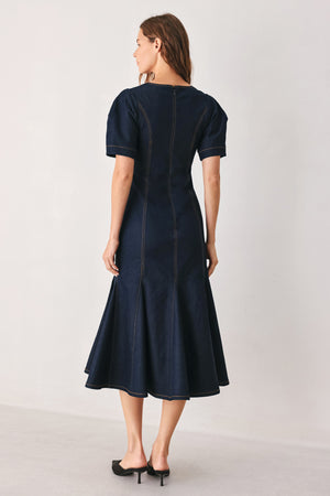 A woman wearing a dark navy blue denim midi dress with short puff sleeves, a V-neckline, and a flared skirt | FREEMARKET