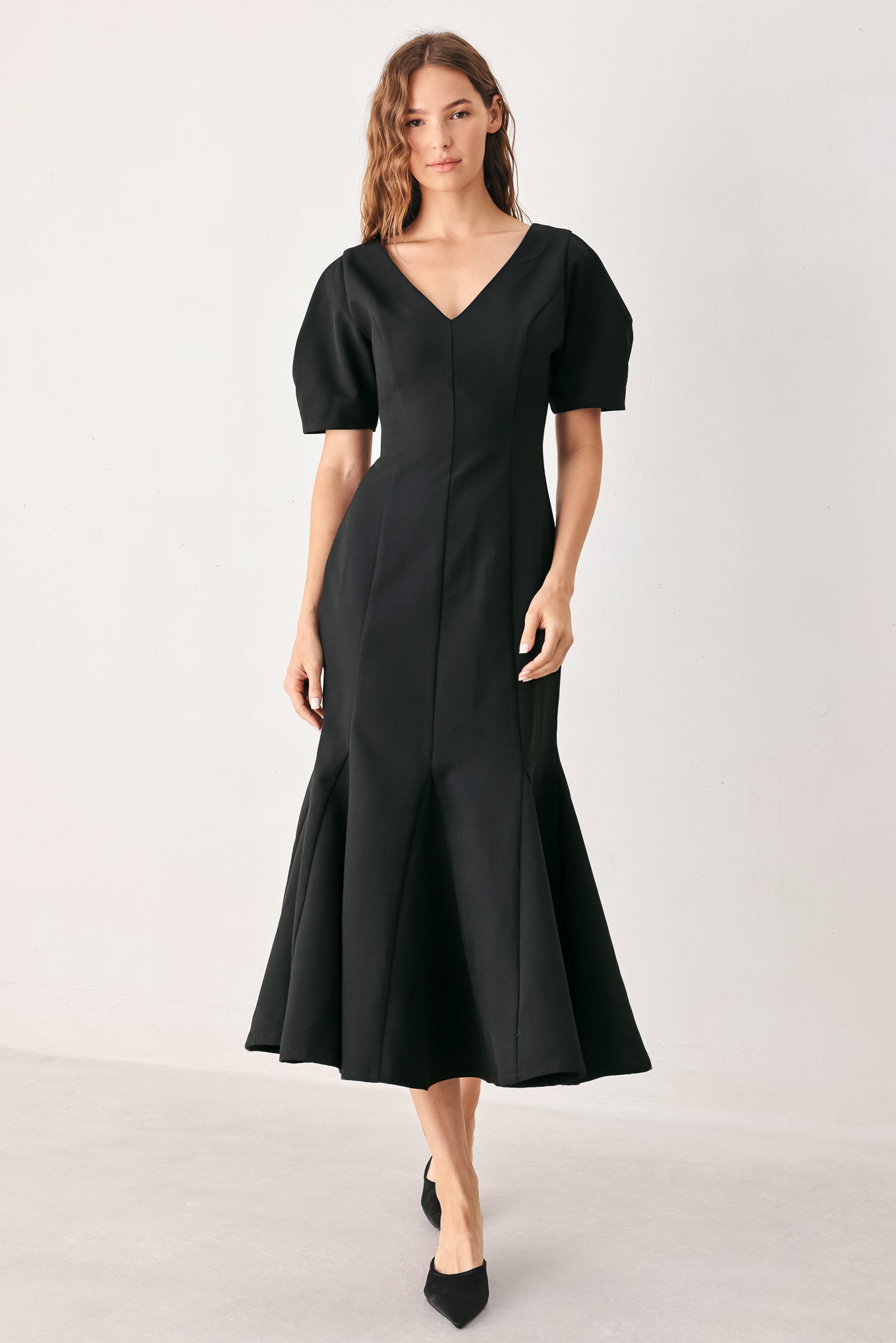 A woman wearing a black midi dress with short puff sleeves, a V-neckline, and a flared hem | FREEMARKET