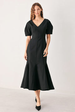 A woman wearing a black midi dress with short puff sleeves, a V-neckline, and a flared hem | FREEMARKET