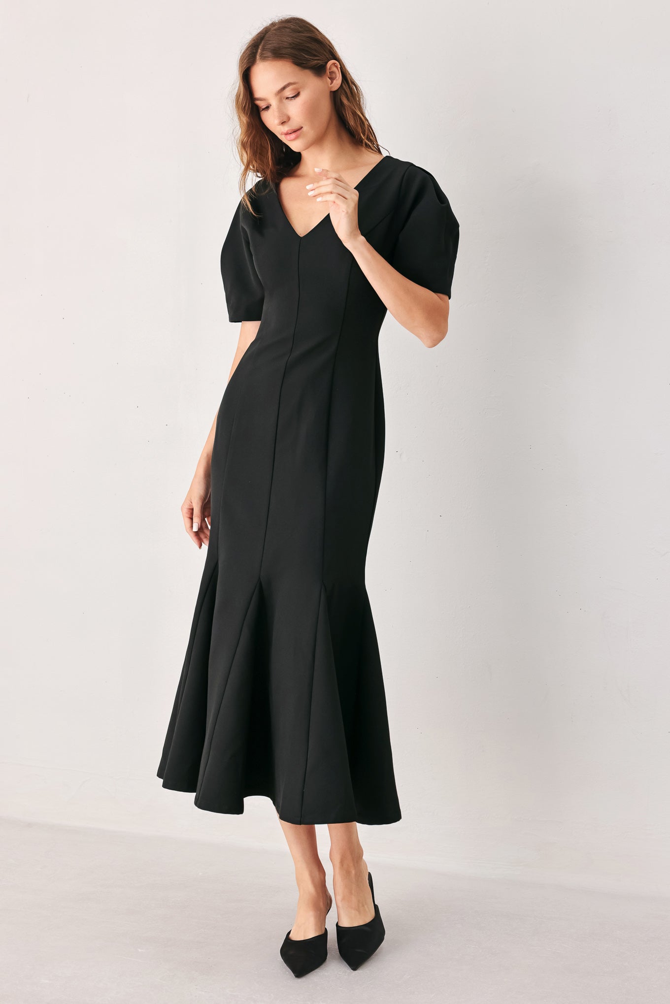 A woman wearing a black midi dress with short puff sleeves, a V-neckline, and a flared hem | FREEMARKET