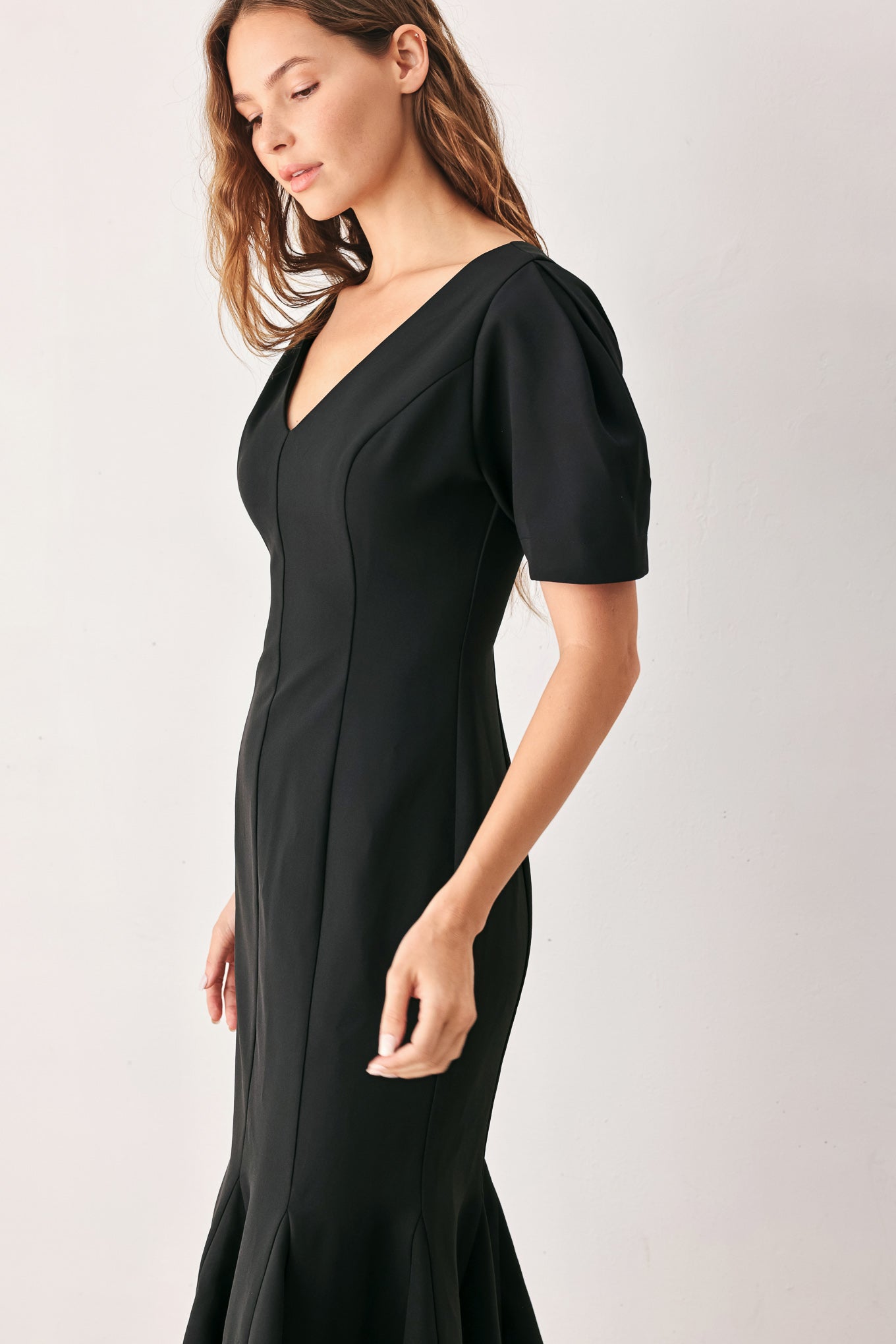 A woman wearing a black midi dress with short puff sleeves, a V-neckline, and a flared hem | FREEMARKET