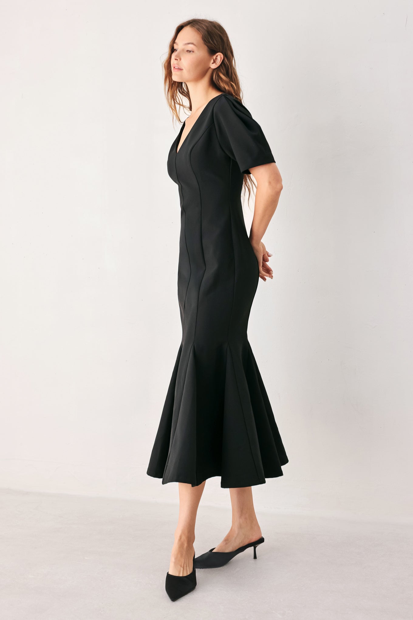 A woman wearing a black midi dress with short puff sleeves, a V-neckline, and a flared hem | FREEMARKET