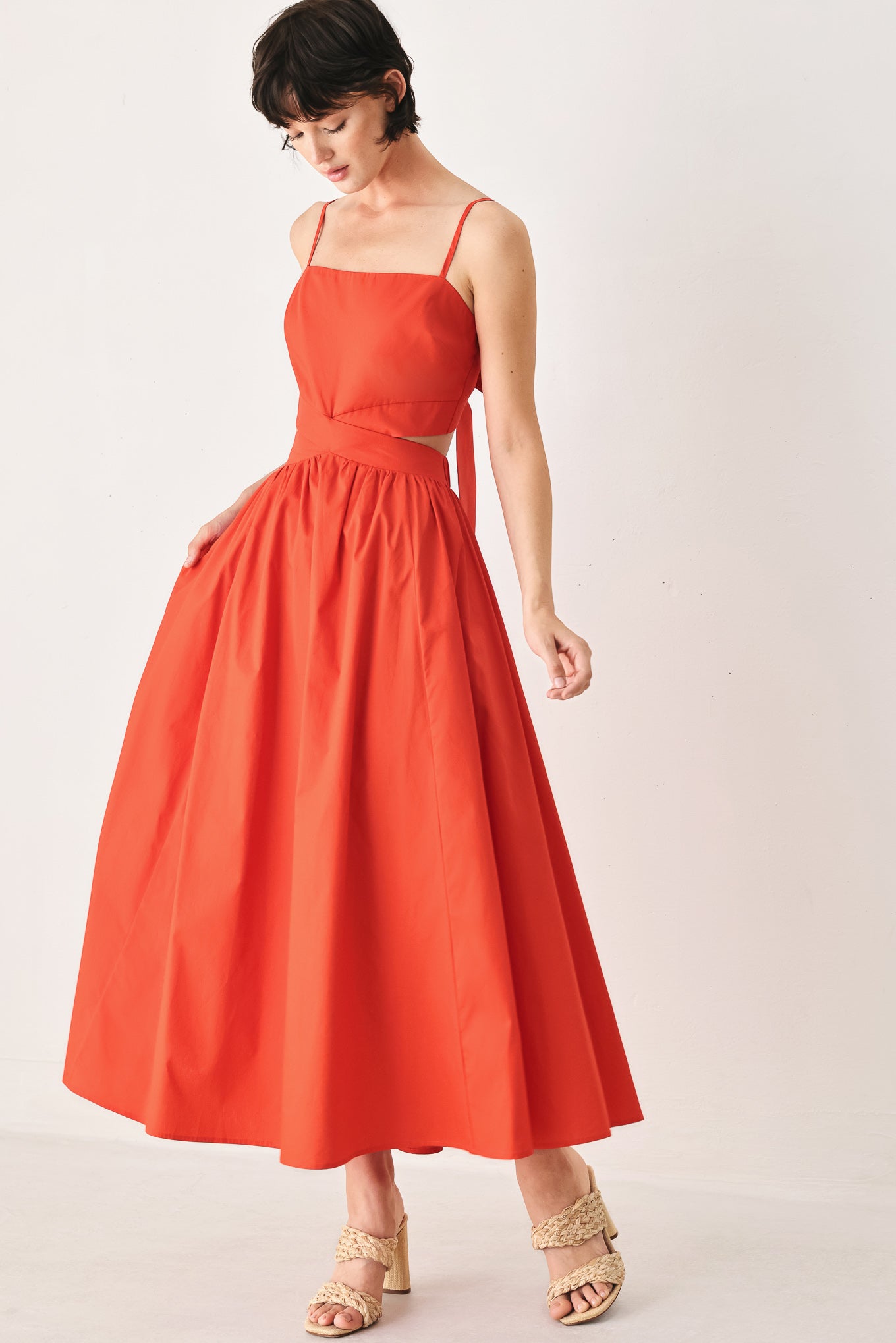 Woman wearing a red midi dress featuring straight neckline, straps, waist cutout, full skirt, and tie detail | FREEMARKET