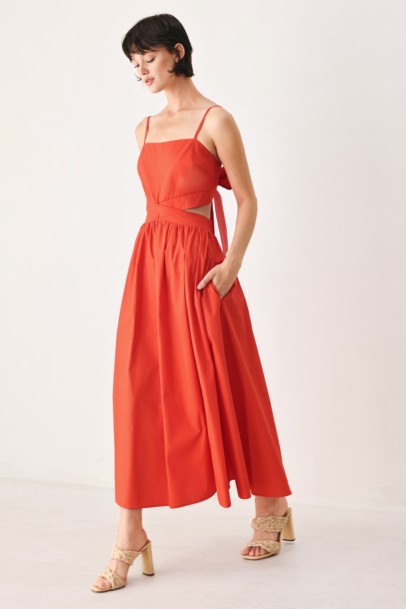 Woman wearing a red midi dress featuring straight neckline, straps, waist cutout, full skirt, and tie detail | FREEMARKET