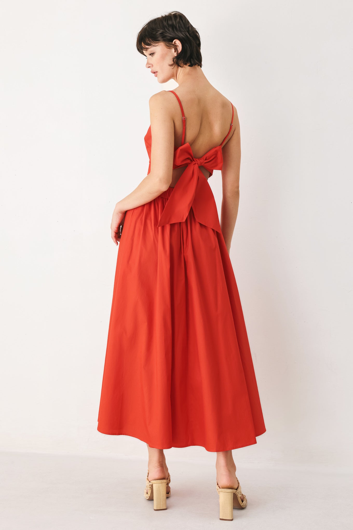 Woman wearing a red midi dress featuring straight neckline, straps, waist cutout, full skirt, and tie detail | FREEMARKET