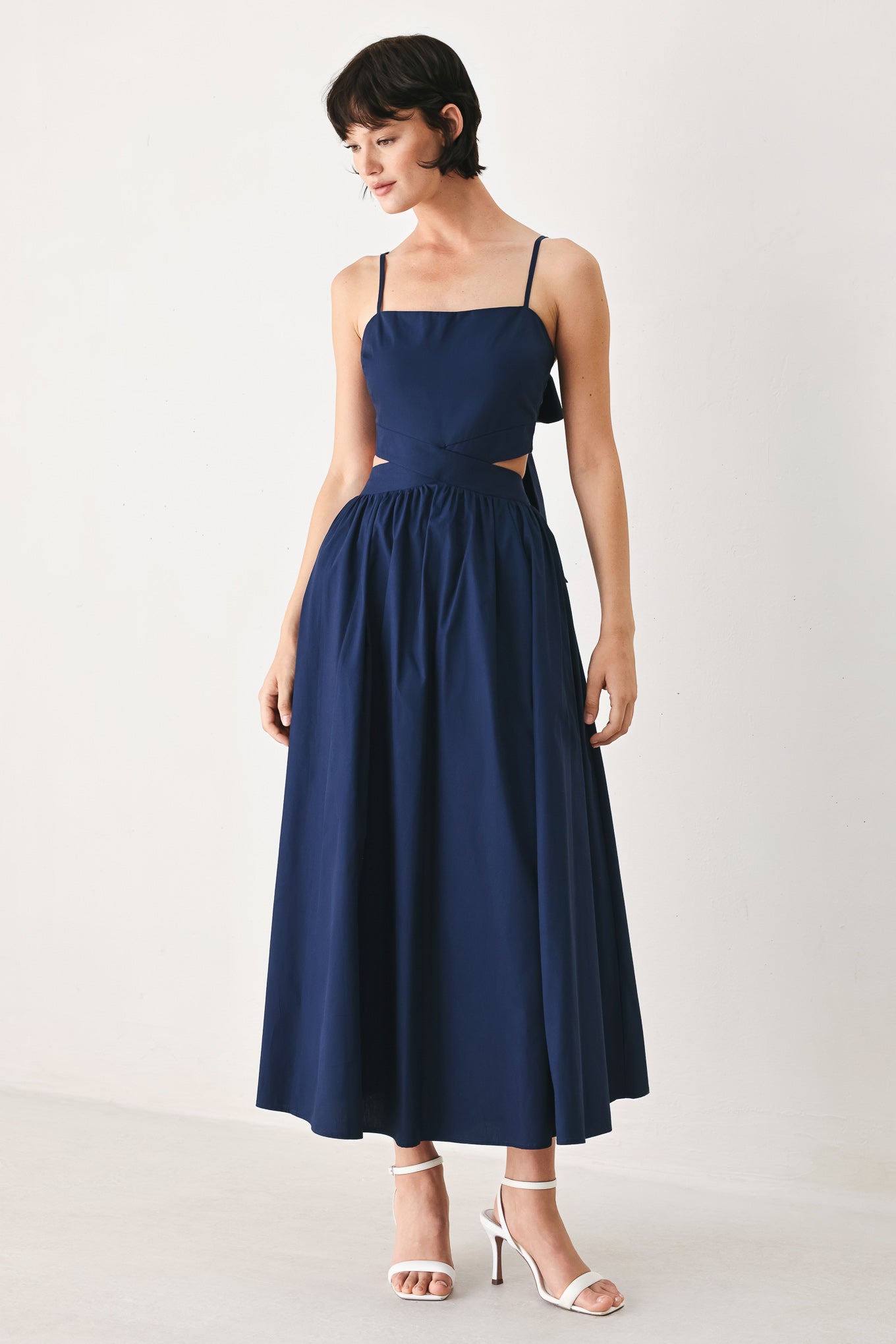 Woman wearing a navy midi dress featuring straight neckline, straps, waist cutout, full skirt, and tie detail | FREEMARKET