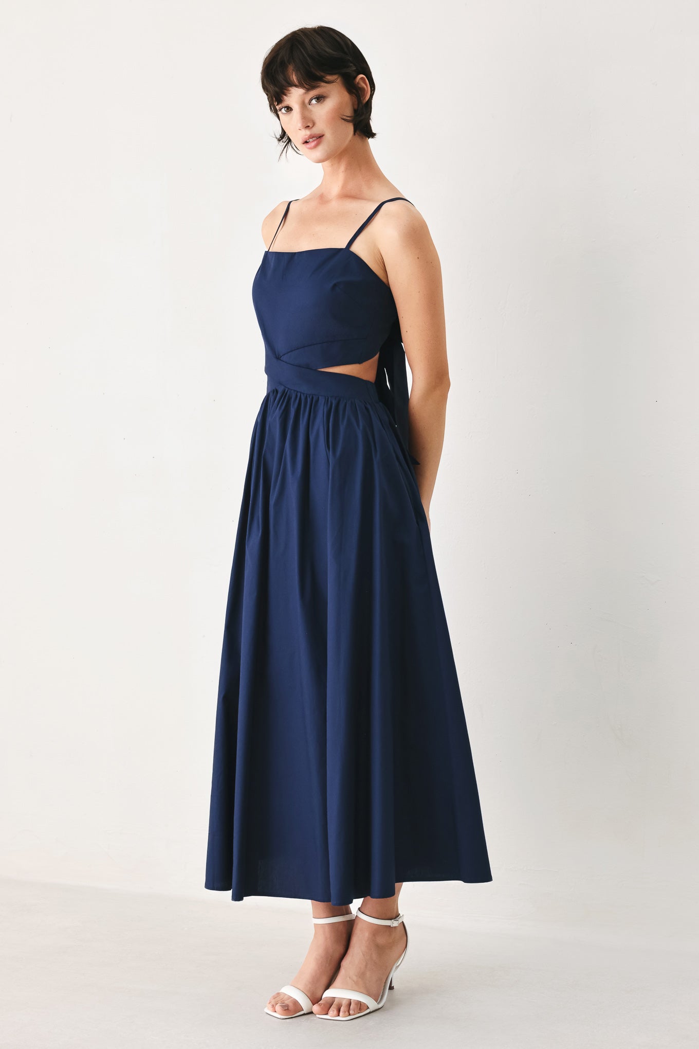 Woman wearing a navy midi dress featuring straight neckline, straps, waist cutout, full skirt, and tie detail | FREEMARKET